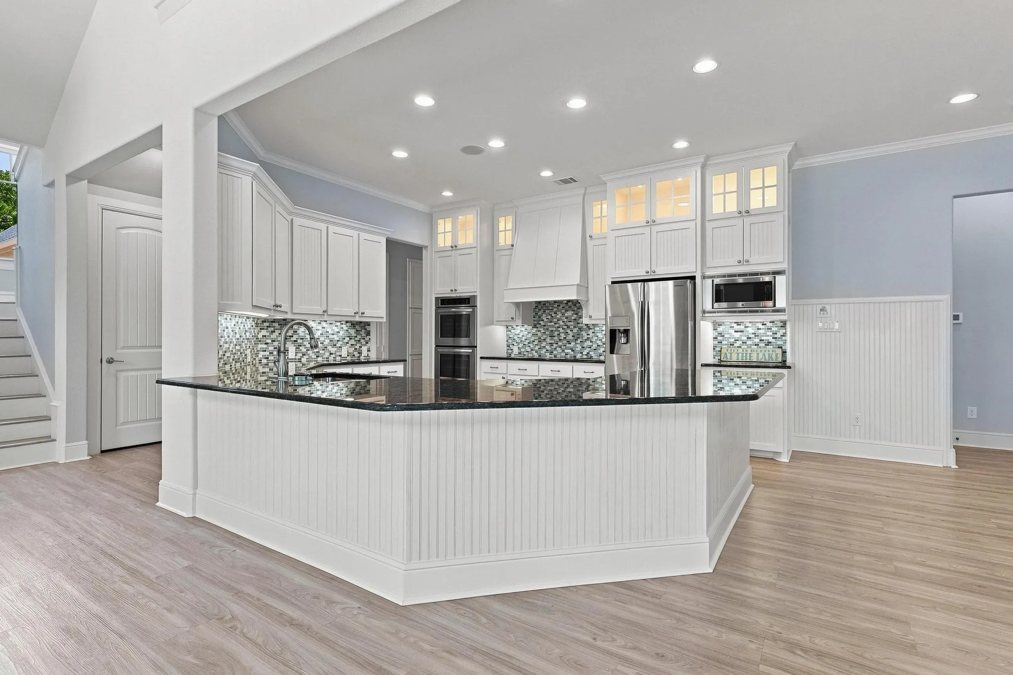 Kitchen featuring an oversized island, wood-finish flooring, white cabinetry, a mosaic tile backsplash, and recessed lighting