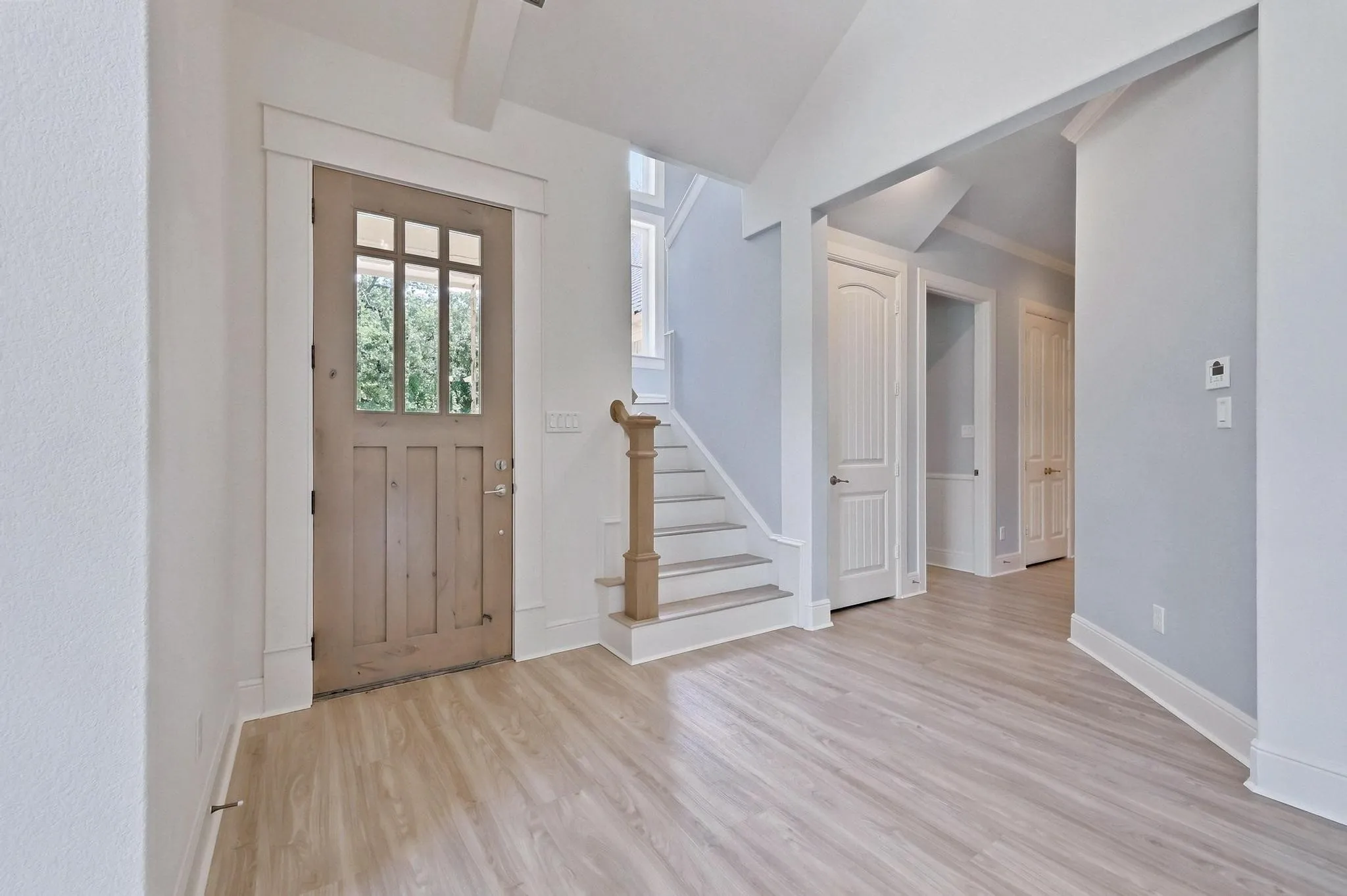 Wood-finish flooring throughout, framed entry door with transom windows, and a staircase with a wood handrail