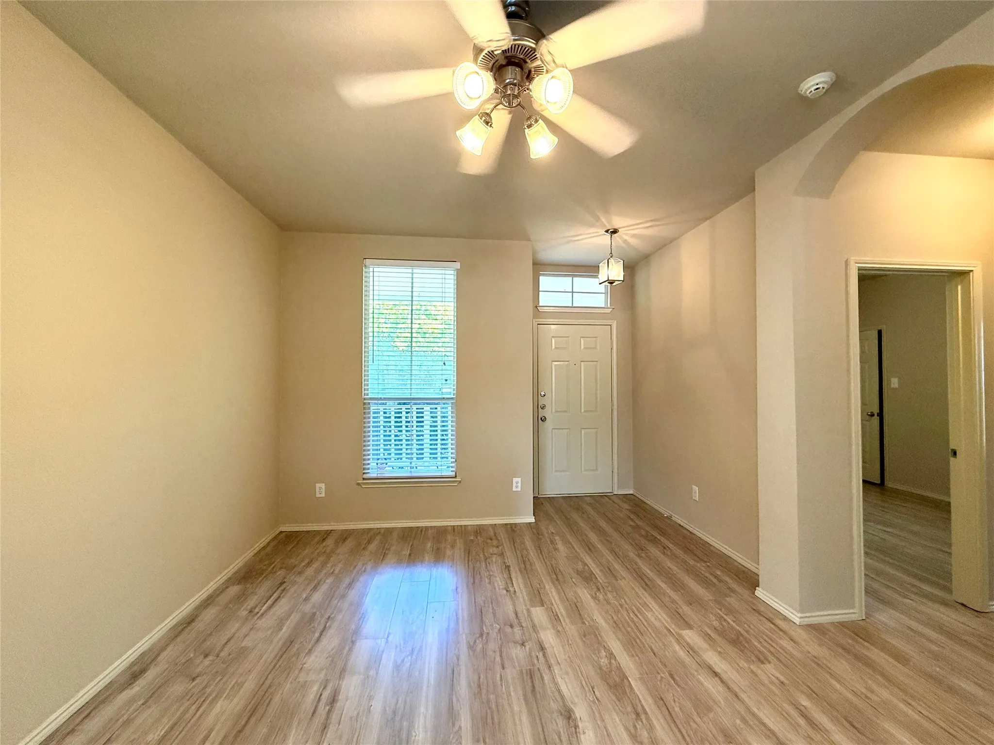Wood-finish flooring throughout, ceiling fan with integrated lighting, transom window over entry door, arched entryway