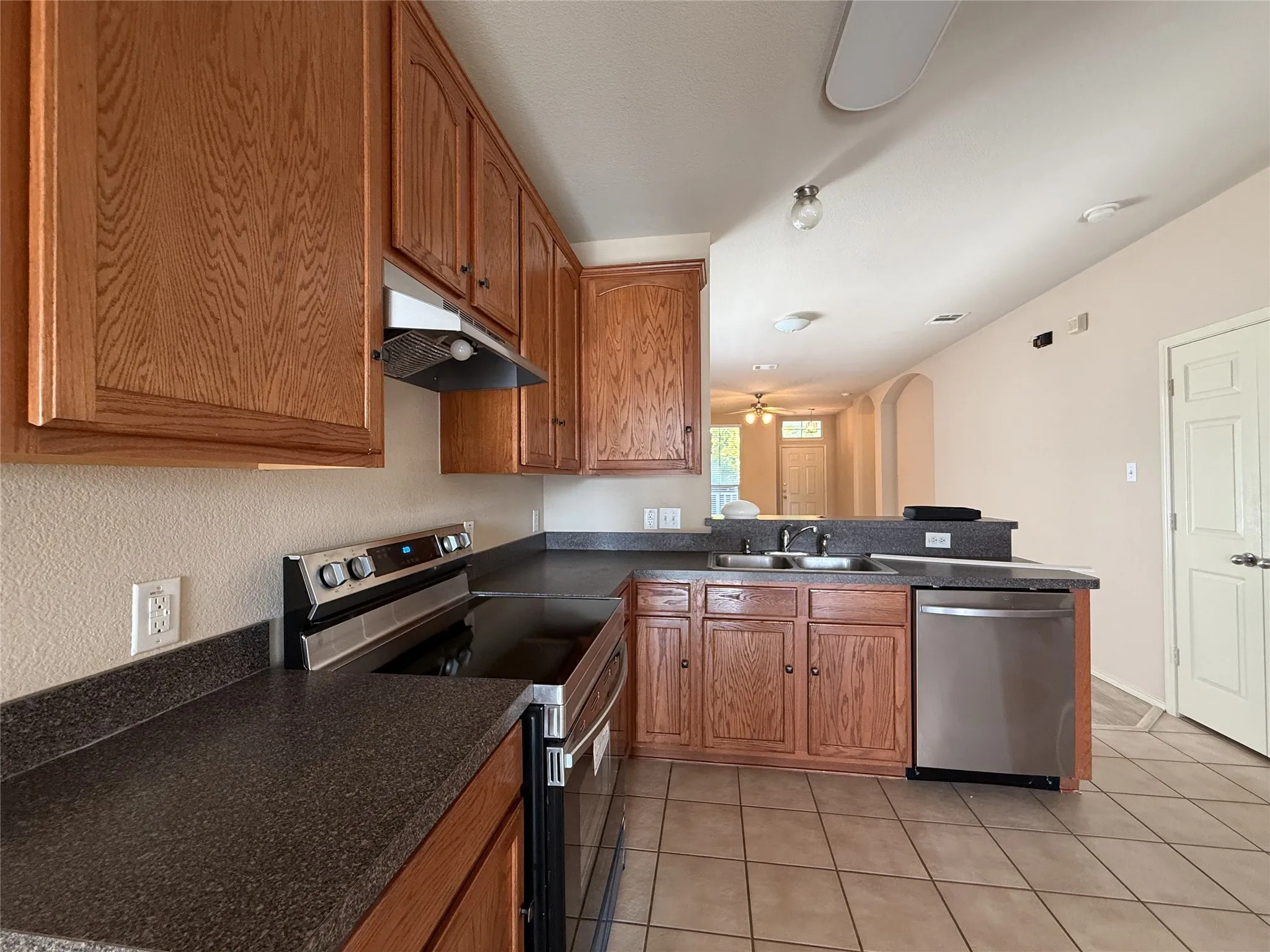 Kitchen featuring wood cabinetry, dark countertops, tile flooring, and stainless steel appliances