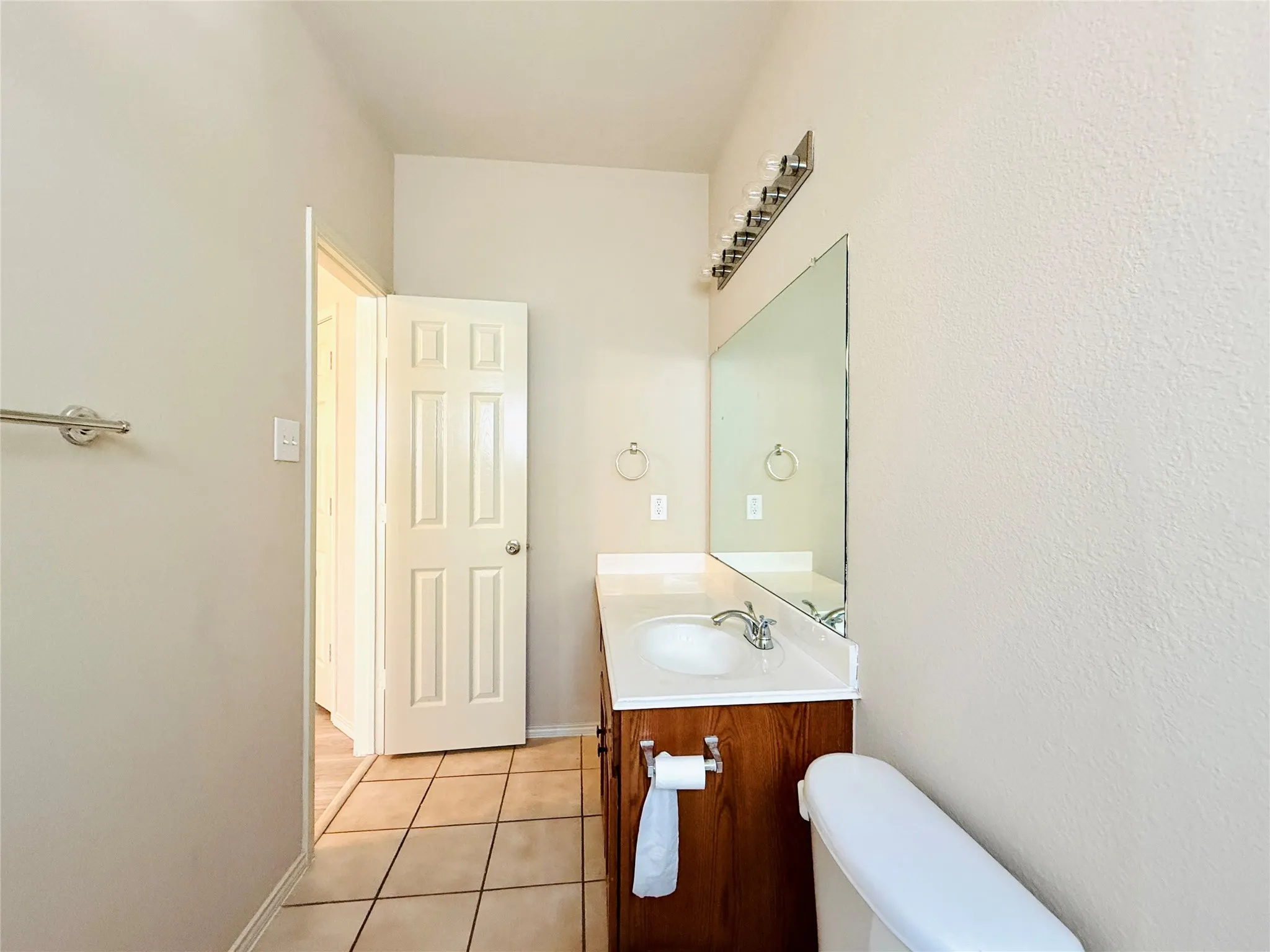 Pedestal sink with chrome faucet, wood-finish vanity, large wall mirror, and tile flooring