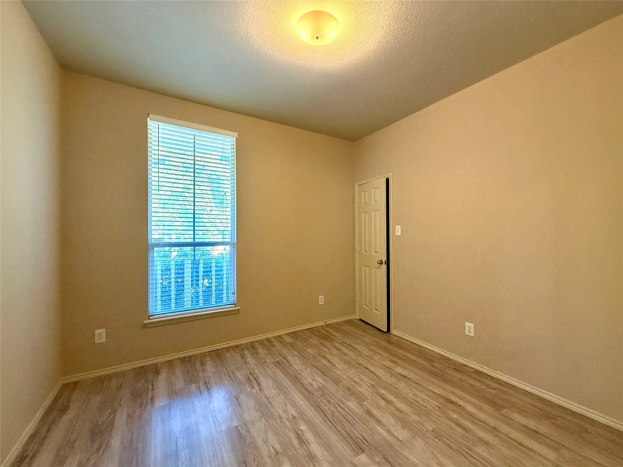 Wood-finish flooring with neutral wall tones and a single window with blinds