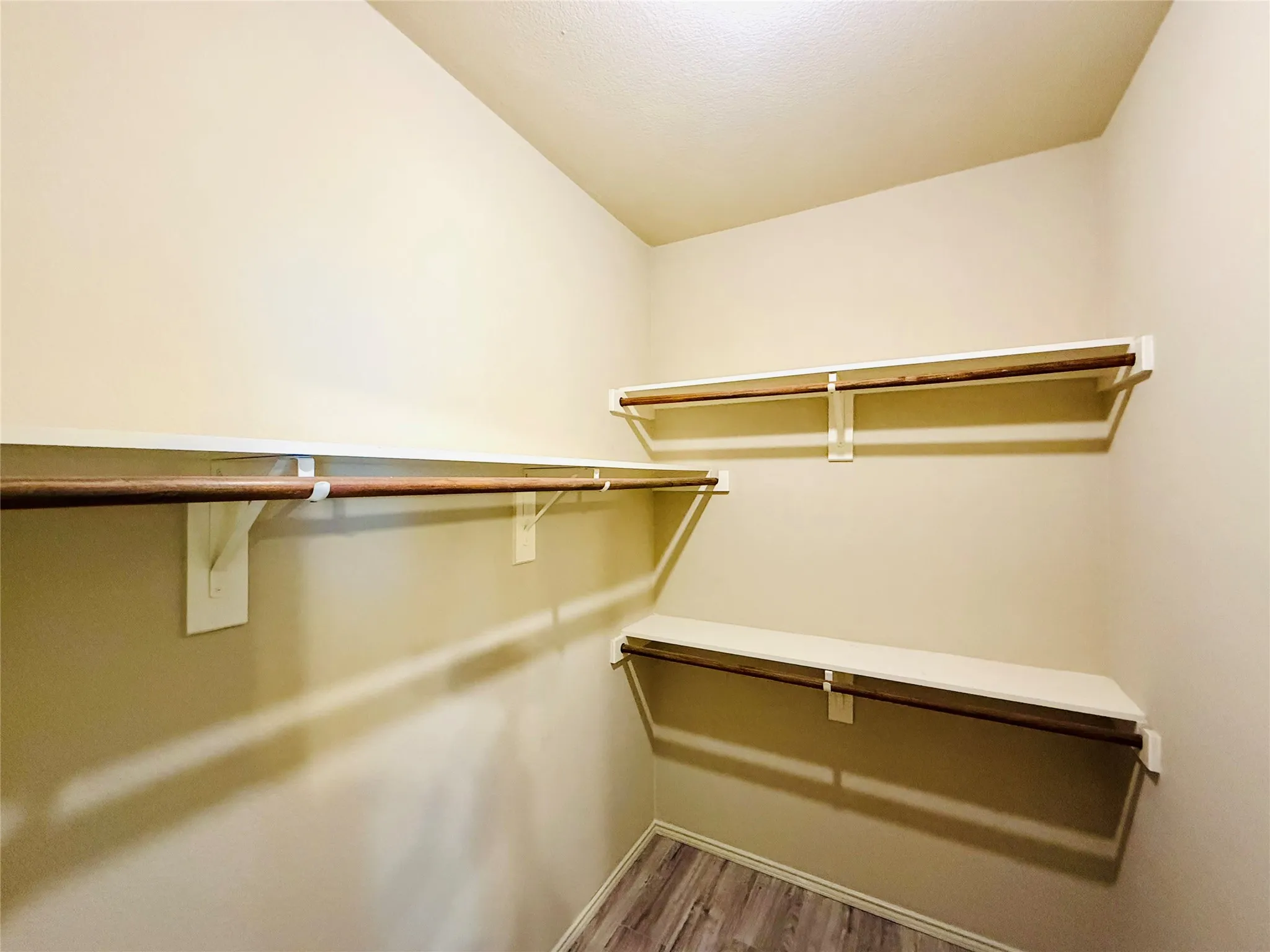 Spacious closet with multiple shelving units and hanging rods, featuring wood-finish flooring