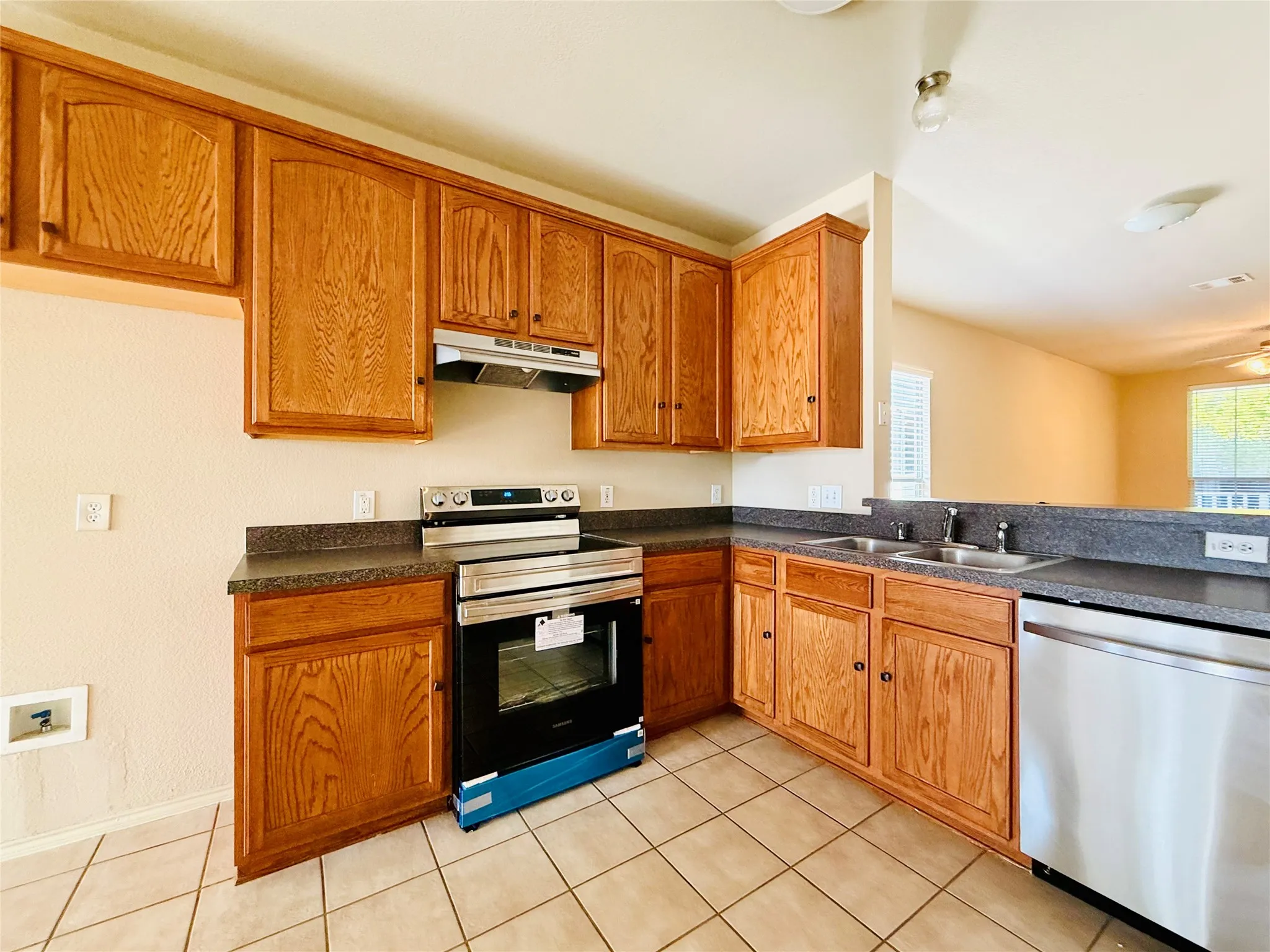 Kitchen featuring wood-finish cabinetry, stainless steel range, stainless steel dishwasher, double basin sink, and tile flooring