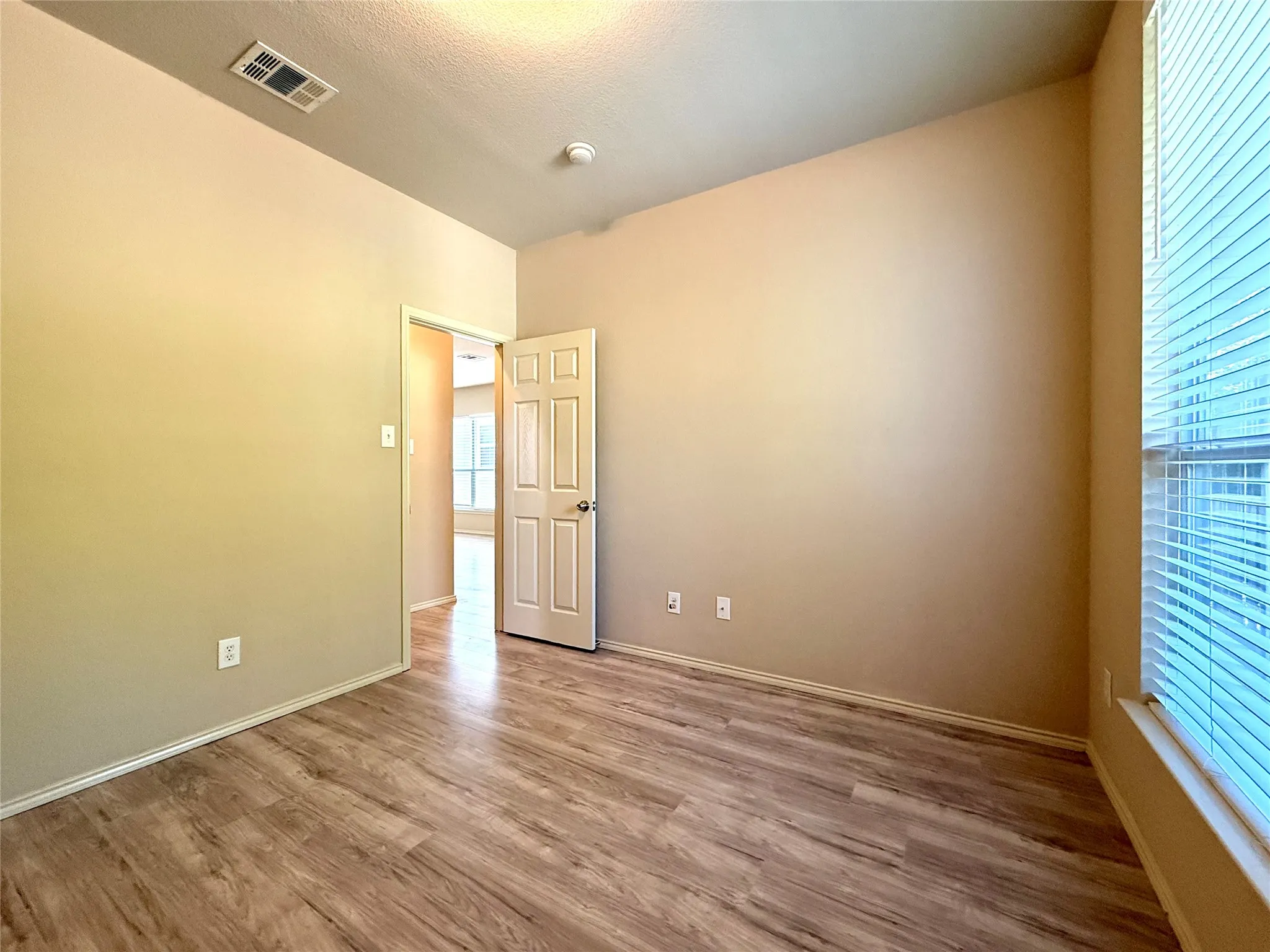 Wood-finish flooring, neutral wall tones, window with blinds, recessed ceiling light, and interior doorway