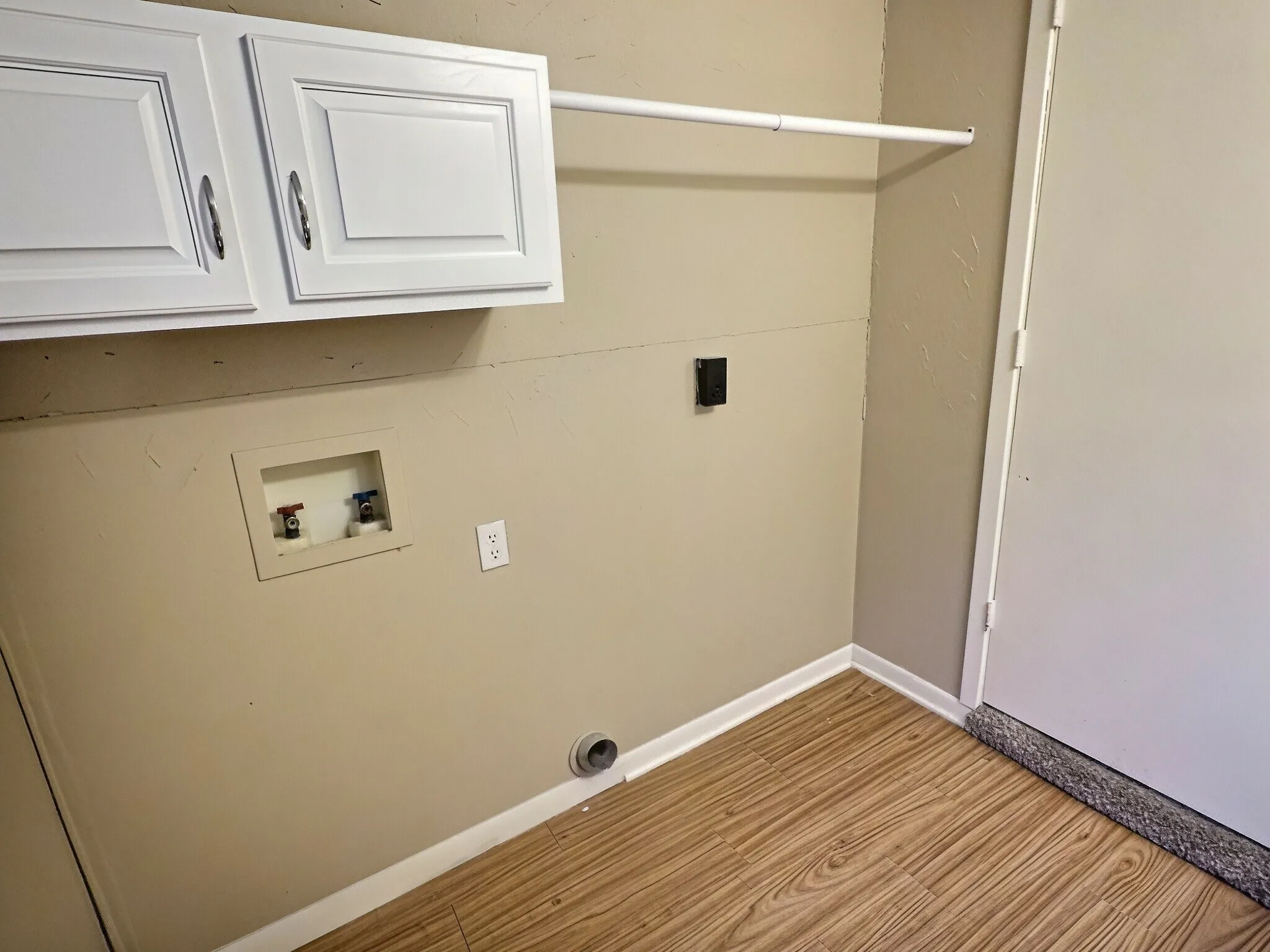 Wood-finish flooring with white trim, white upper cabinetry, and a laundry hookup station
