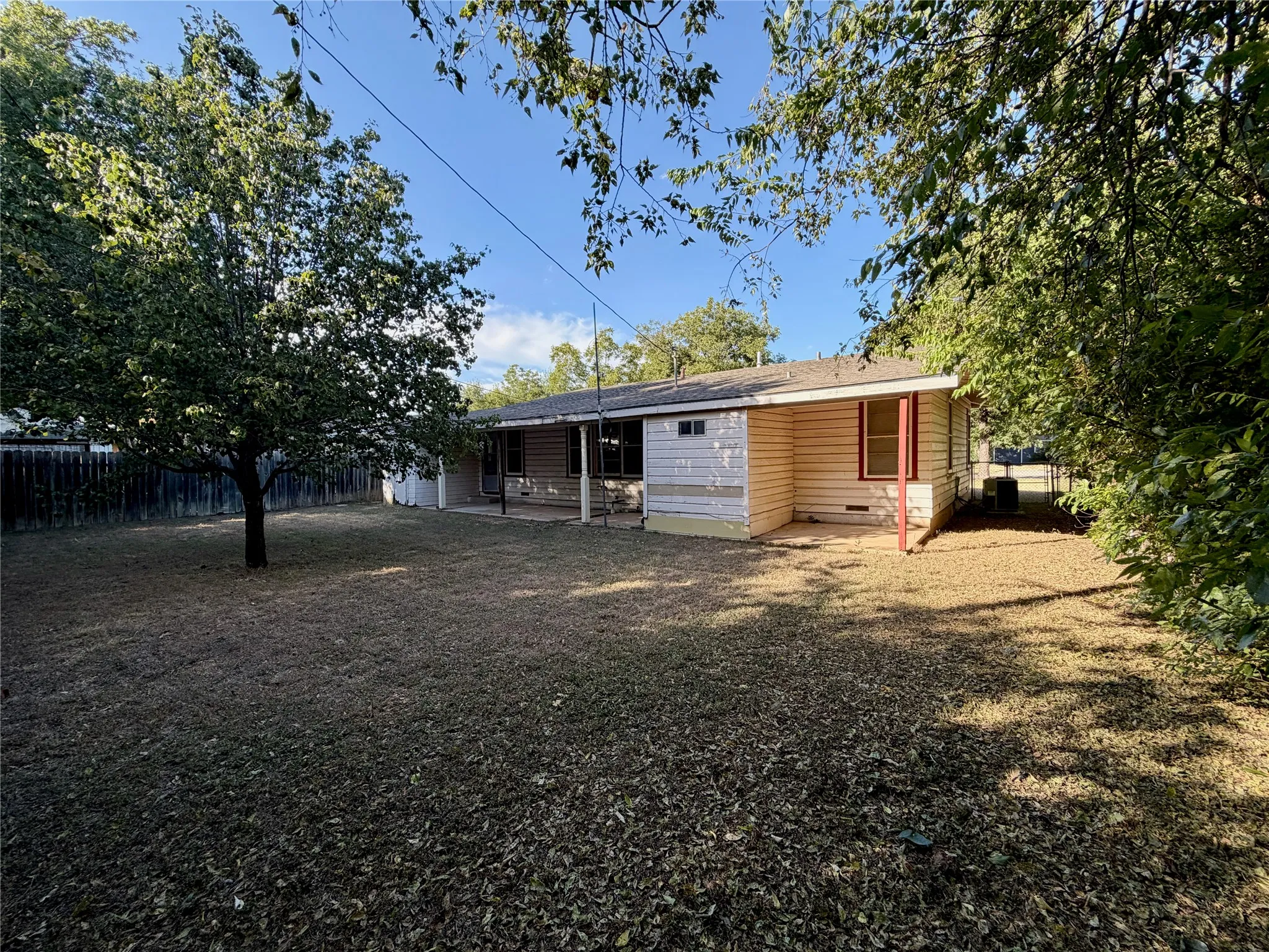 Expansive rear yard featuring a privacy fence, mature trees, and a covered patio area