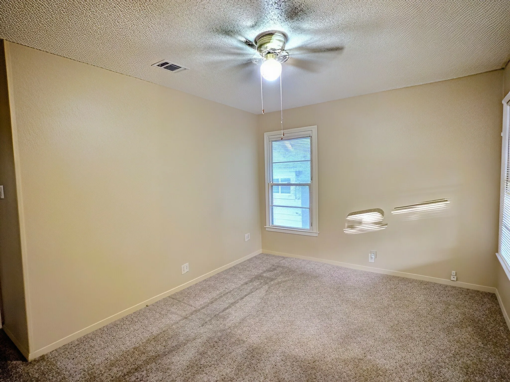 Textured carpet flooring, neutral painted walls, single window, and ceiling fan with light fixture