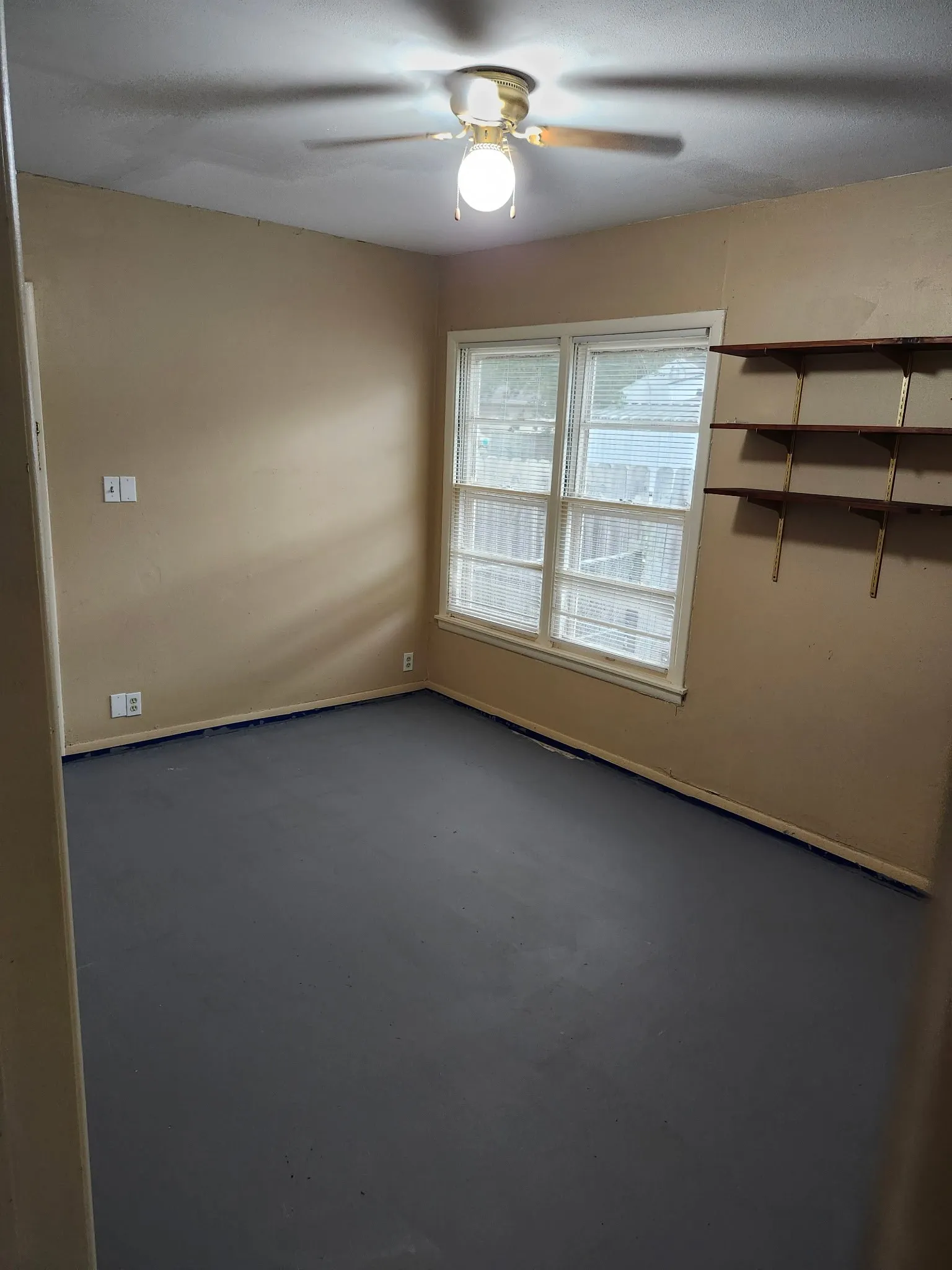 Ceiling fan with light fixture, window with white blinds, built-in wall shelving, and painted flooring