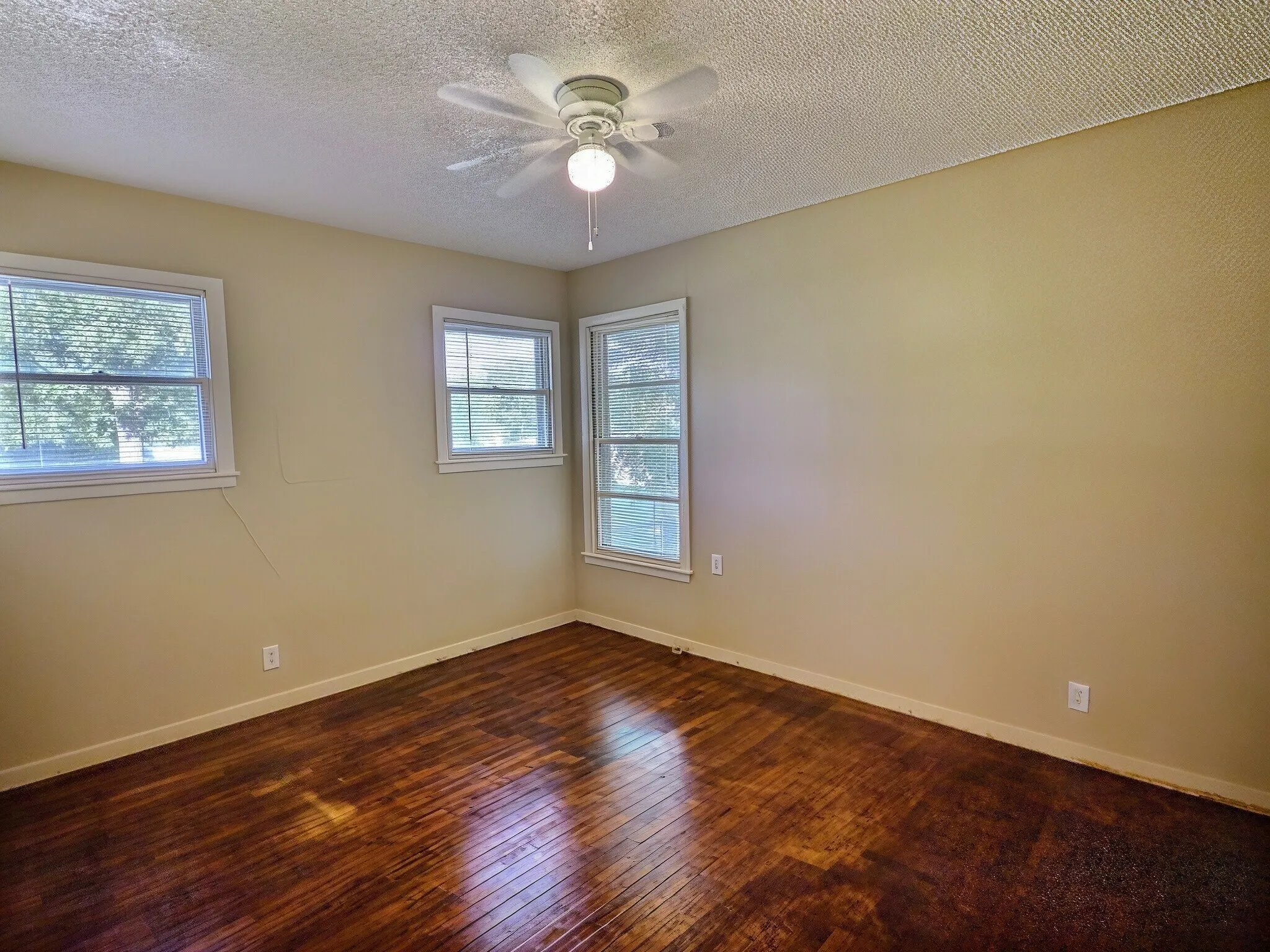 Wood-finish flooring, multiple windows, ceiling fan with integrated lighting, and neutral wall tones