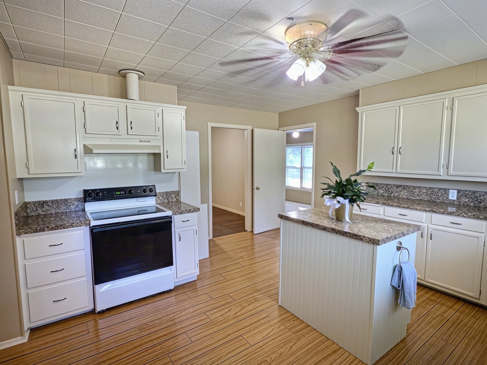 Kitchen featuring wood-finish flooring, white cabinetry, granite-style countertops, a white electric range, and a central island with beadboard paneling