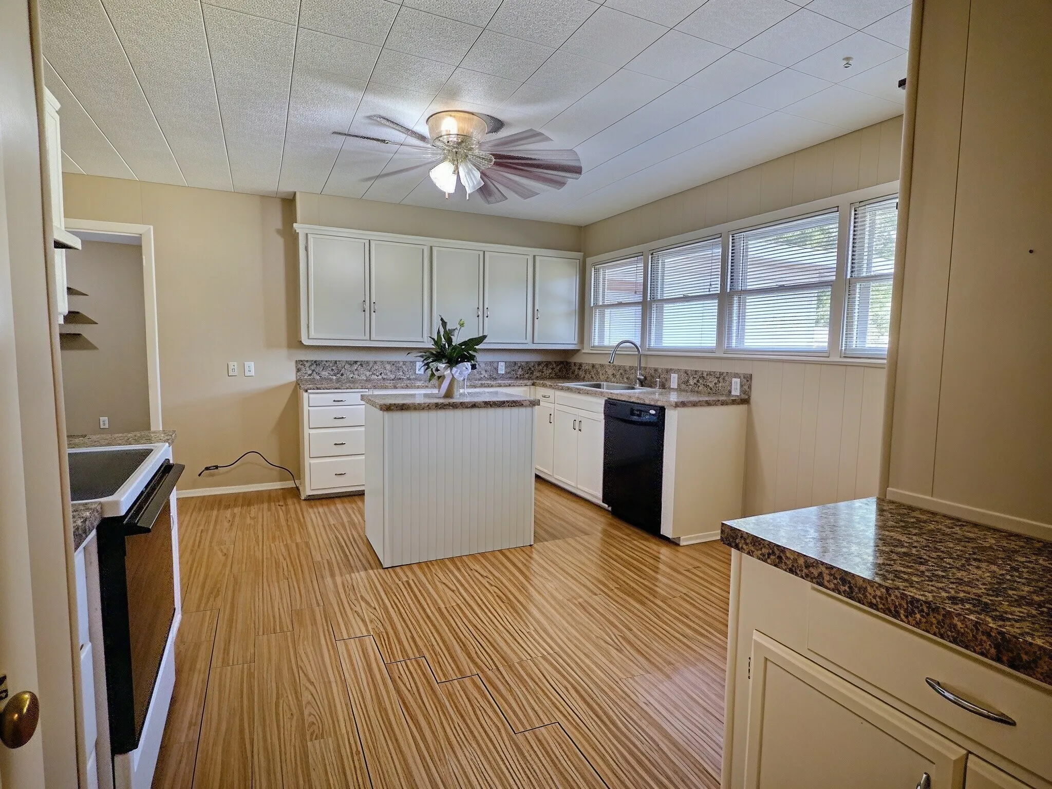 Kitchen featuring wood-finish flooring, white cabinetry, granite-style countertops, a kitchen island, and a ceiling fan