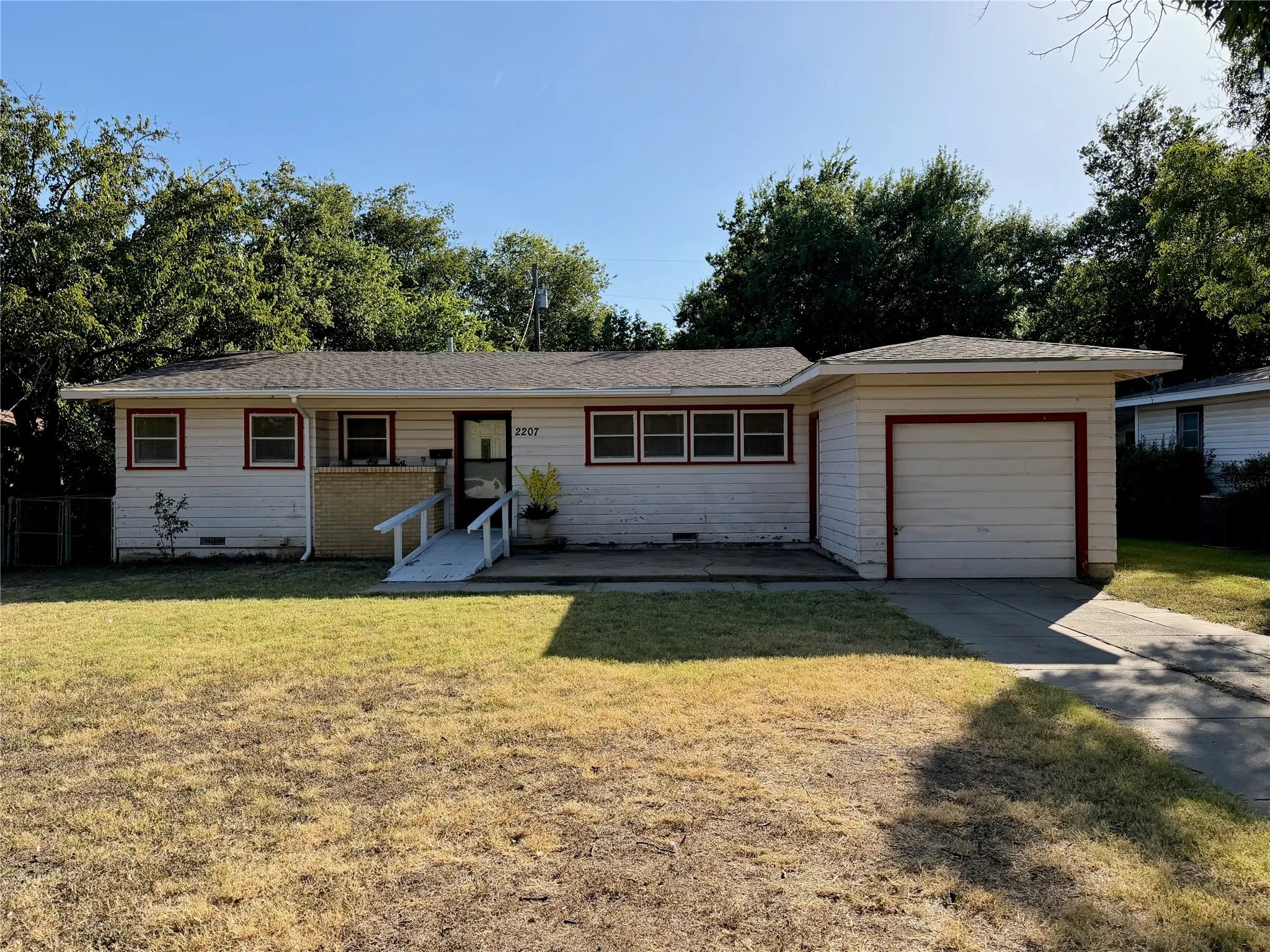 Single-story residence featuring a front lawn, attached garage with a red-trimmed door, and a front entry ramp