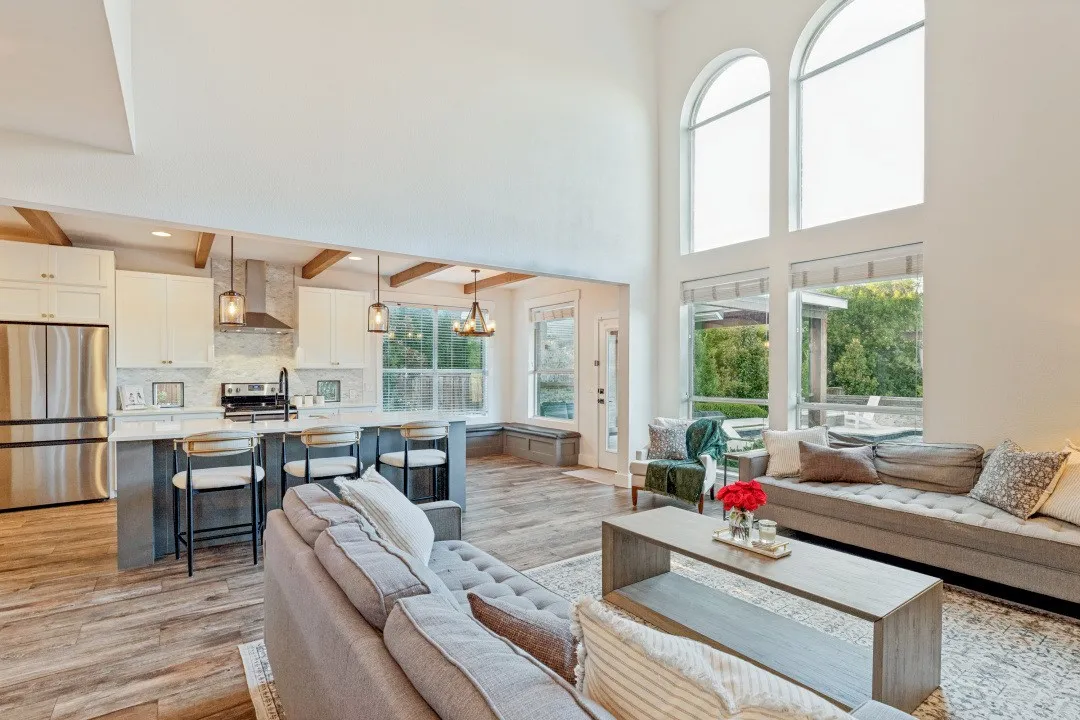 Two-story ceilings, arched windows, wood-finish flooring, exposed ceiling beams, and a kitchen island with seating