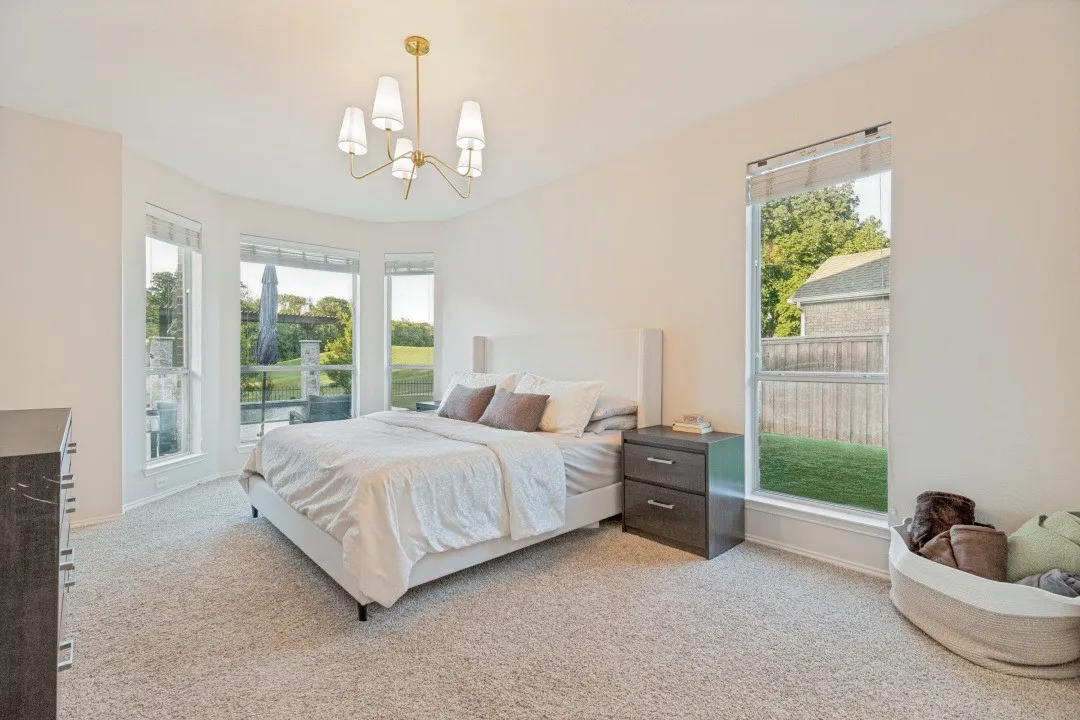 Carpeted room with multiple windows, a decorative chandelier, and a built-in upholstered headboard