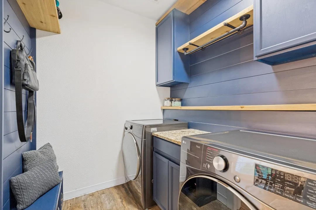 Laundry area featuring wood-finish flooring, blue shiplap accent wall, built-in cabinetry, and open wood shelving