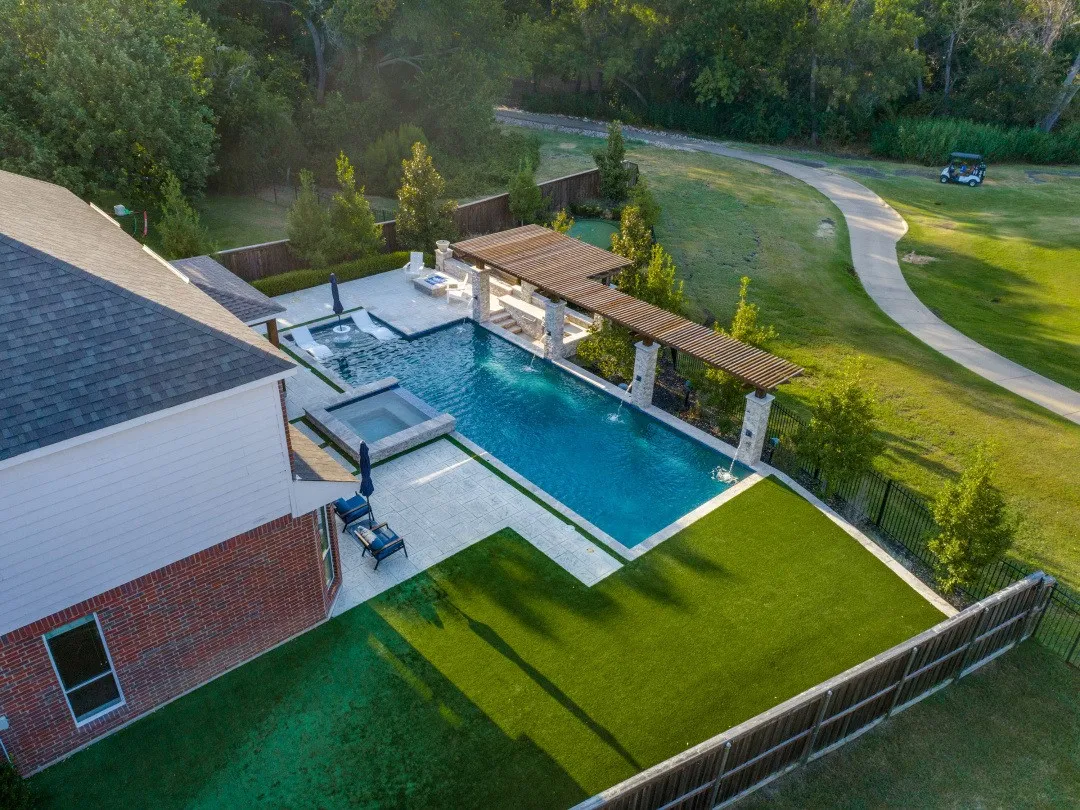 Rectangular swimming pool with integrated spa and water features, surrounded by a light-toned paved patio