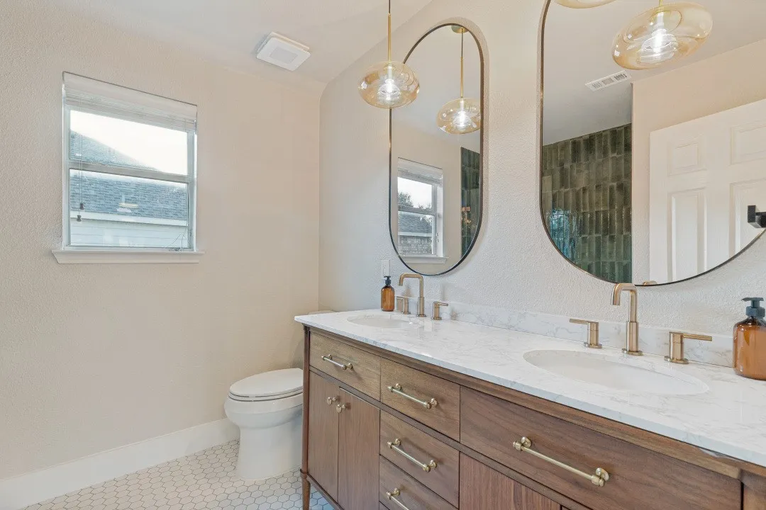 Double vanity with wood-finish cabinetry, white countertop, and dual oval mirrors
