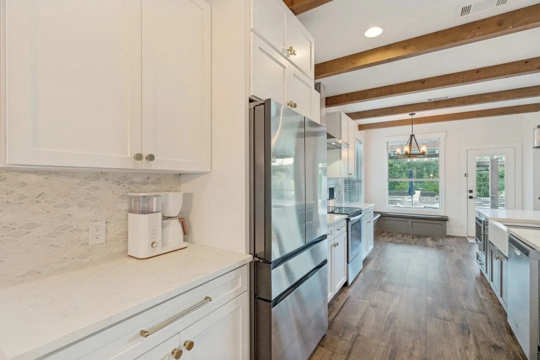 Kitchen featuring wood-finish flooring, exposed wood beams, white cabinetry, stainless steel appliances, and light-toned countertops