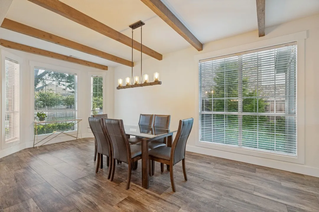 Wood-finish flooring with exposed ceiling beams and a linear chandelier