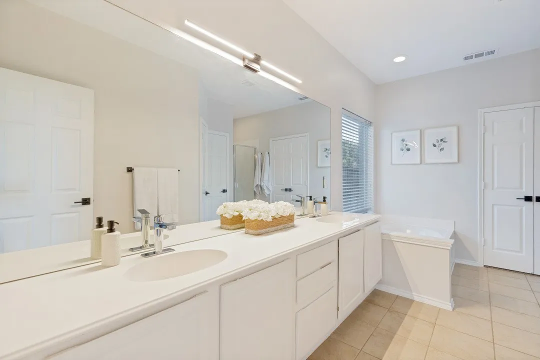 Dual vanity with integrated sinks, expansive wall-mounted mirror, modern linear light fixture, recessed lighting, and a built-in tub