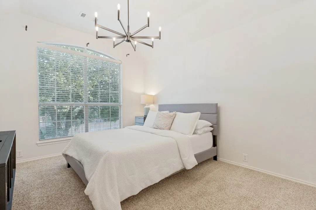 Vaulted ceiling with a contemporary chandelier, arched window with horizontal blinds, and neutral carpeting
