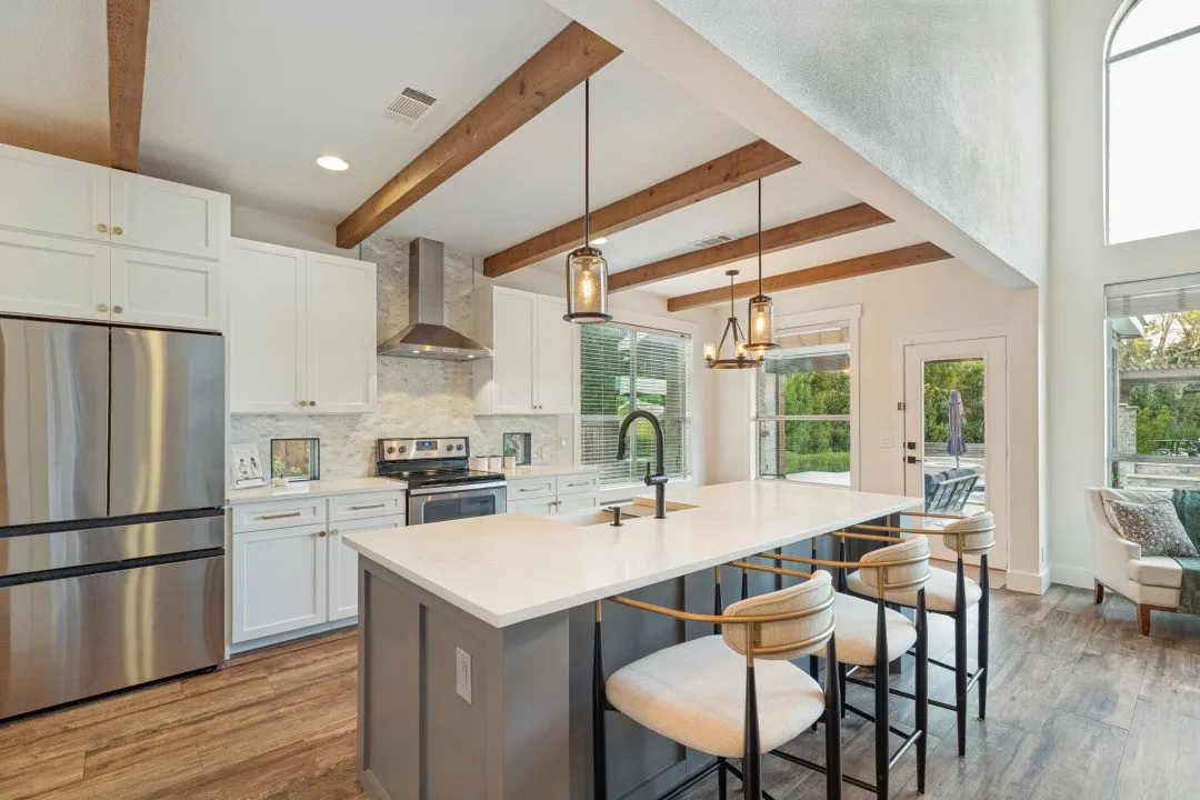 Kitchen featuring wood-finish flooring, exposed wood ceiling beams, white cabinetry, a large kitchen island with counter seating, and stainless steel appliances