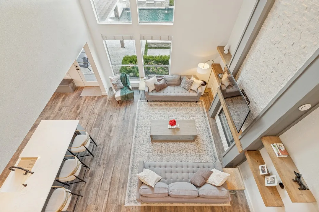 Vaulted ceiling, full-height windows, wood-finish flooring, white quartz island with integrated sink, and a textured white accent wall