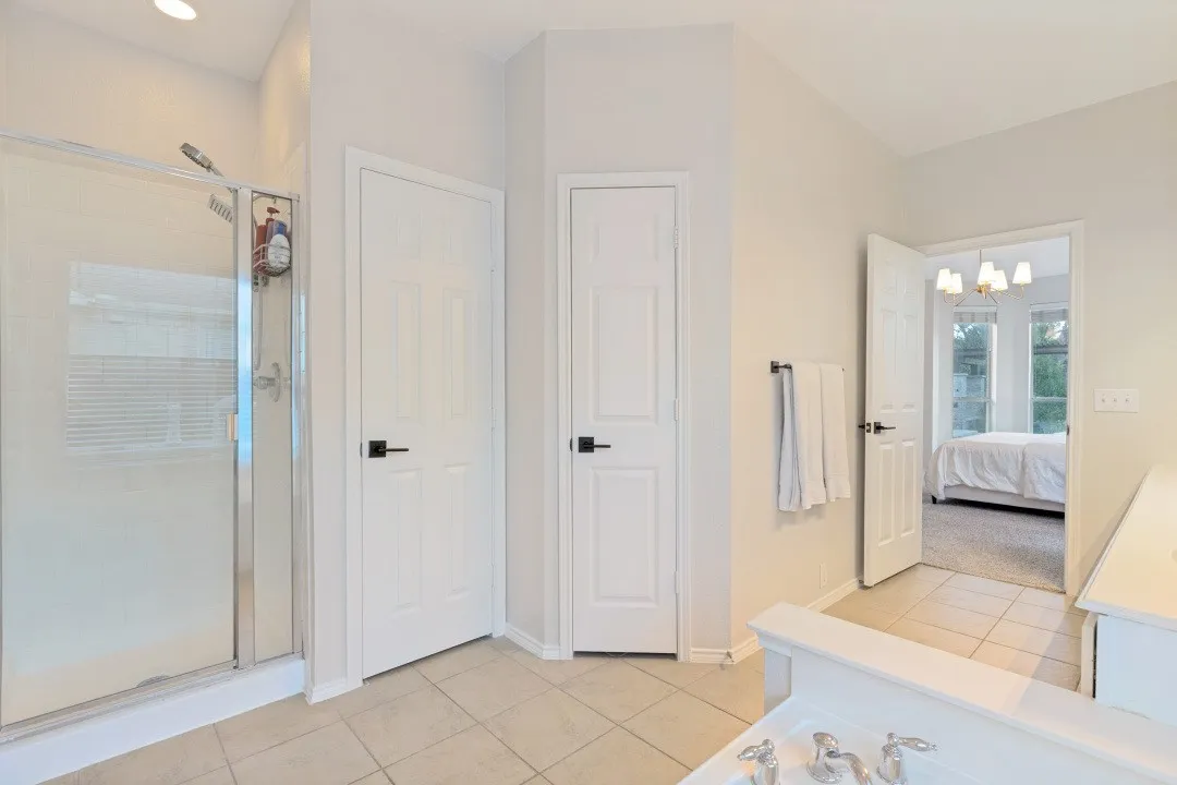 Glass-enclosed shower with a recessed ceiling light, white paneled doors, and square floor tiles