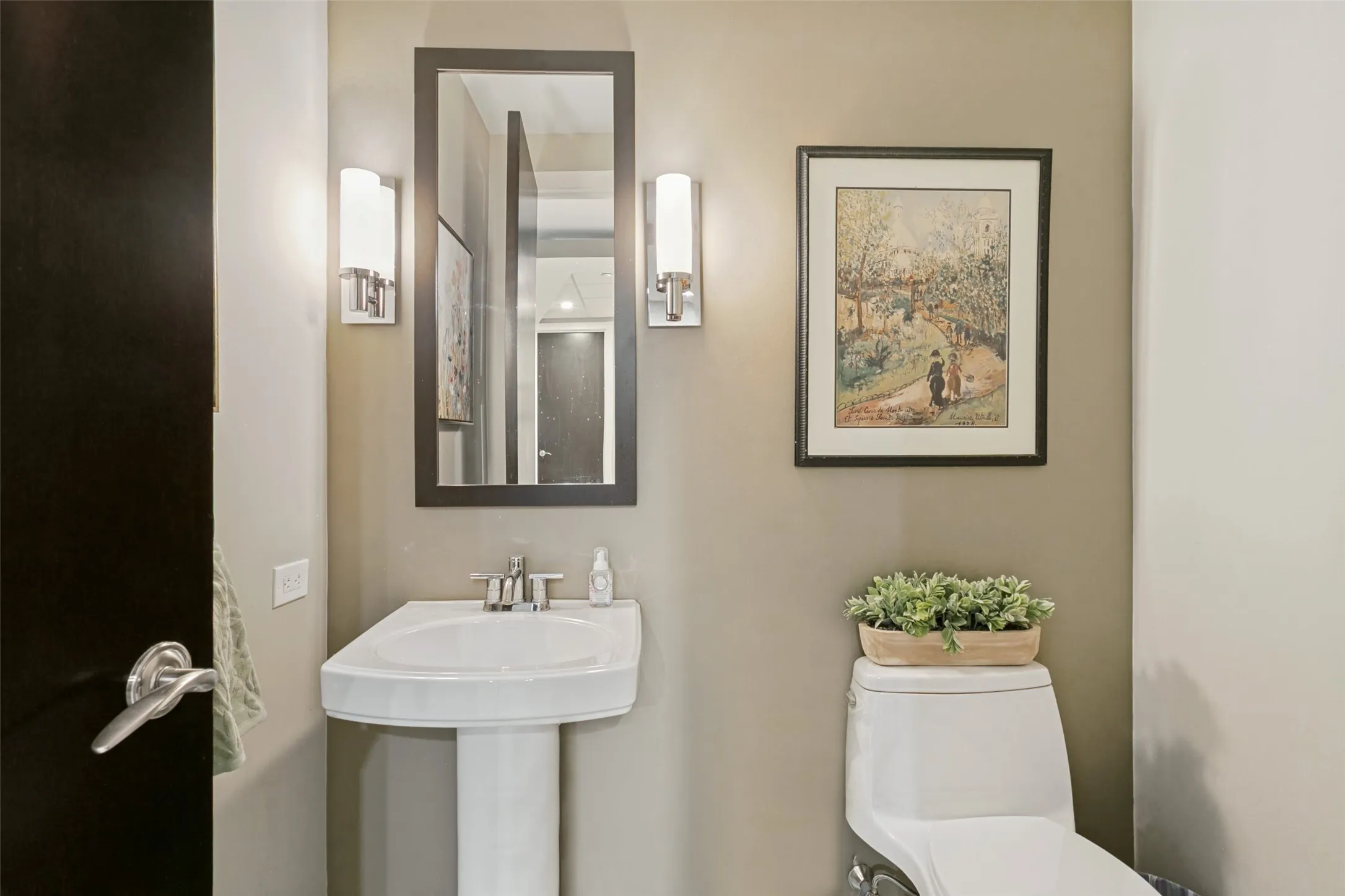 Half bathroom outside of office area. Pedestal sink with chrome faucet, framed mirror, and dual wall sconces