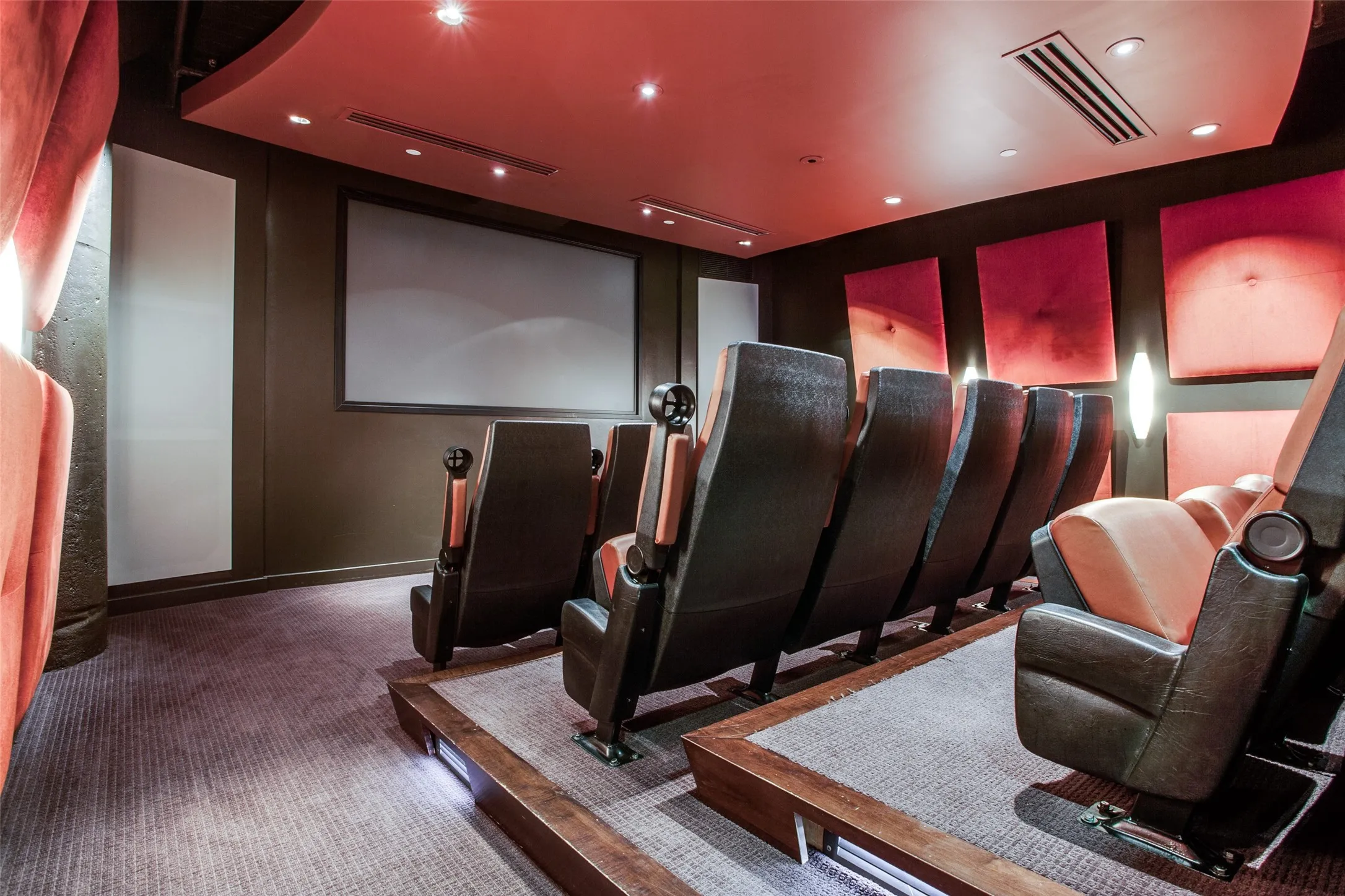Theater featuring a large projection screen, tiered seating with individual armchairs, plush carpet flooring, and recessed ceiling lighting