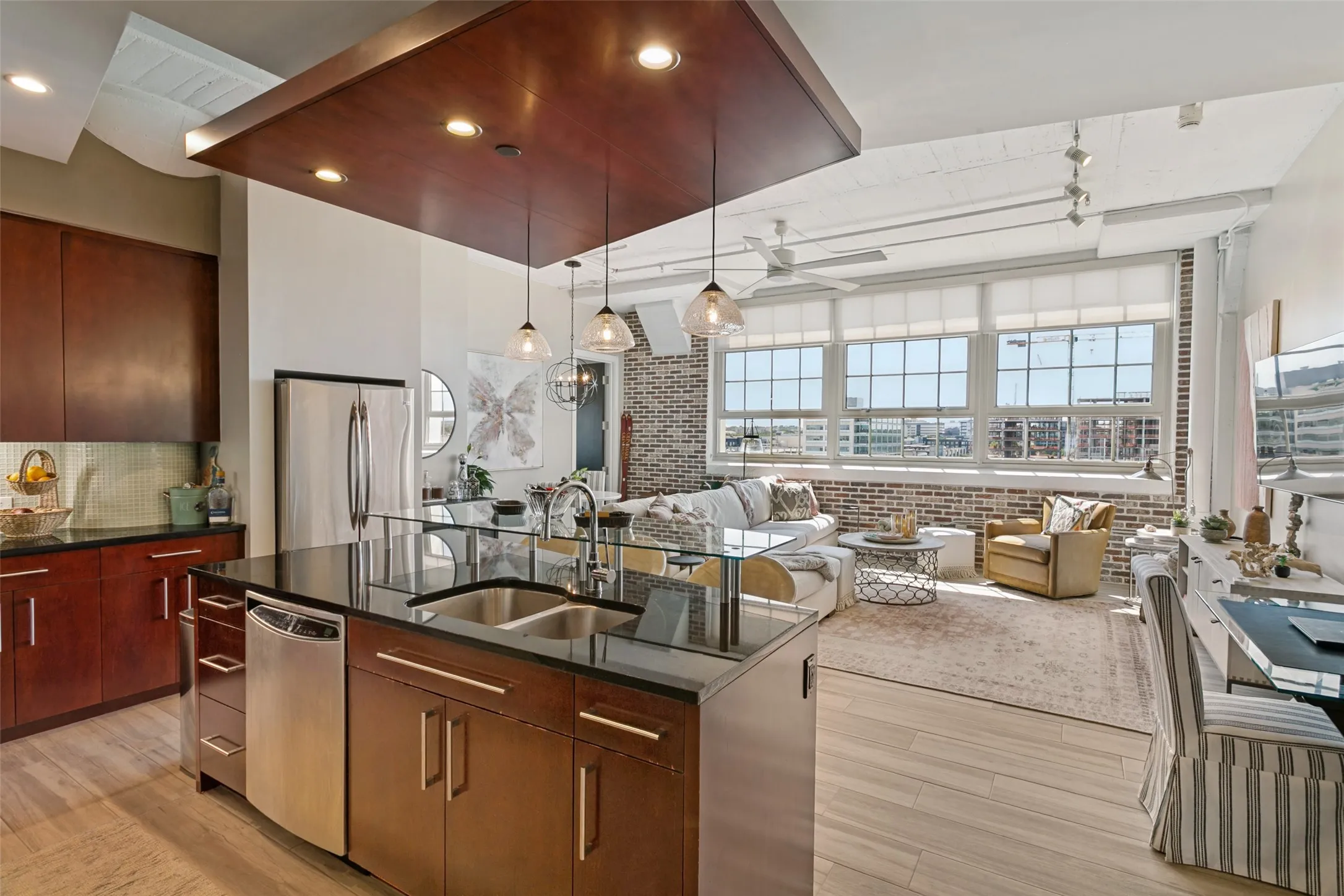 Open-concept living area with porcelain wood-look flooring, exposed brick accents, and large multi-pane windows