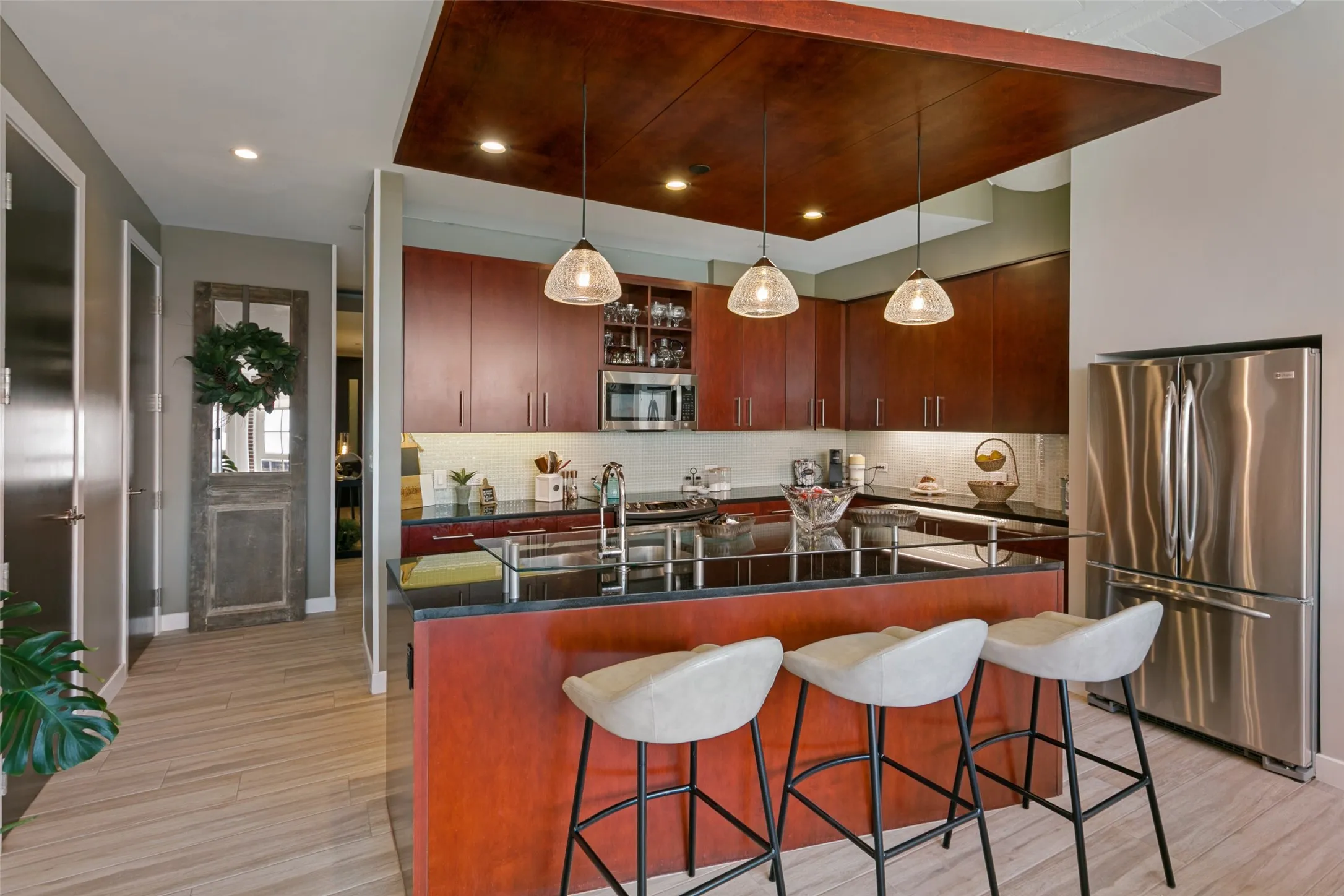 Open kitchen featuring wood-finish cabinetry, stainless steel appliances, dark countertops, and a wood-paneled ceiling accent with pendant lighting