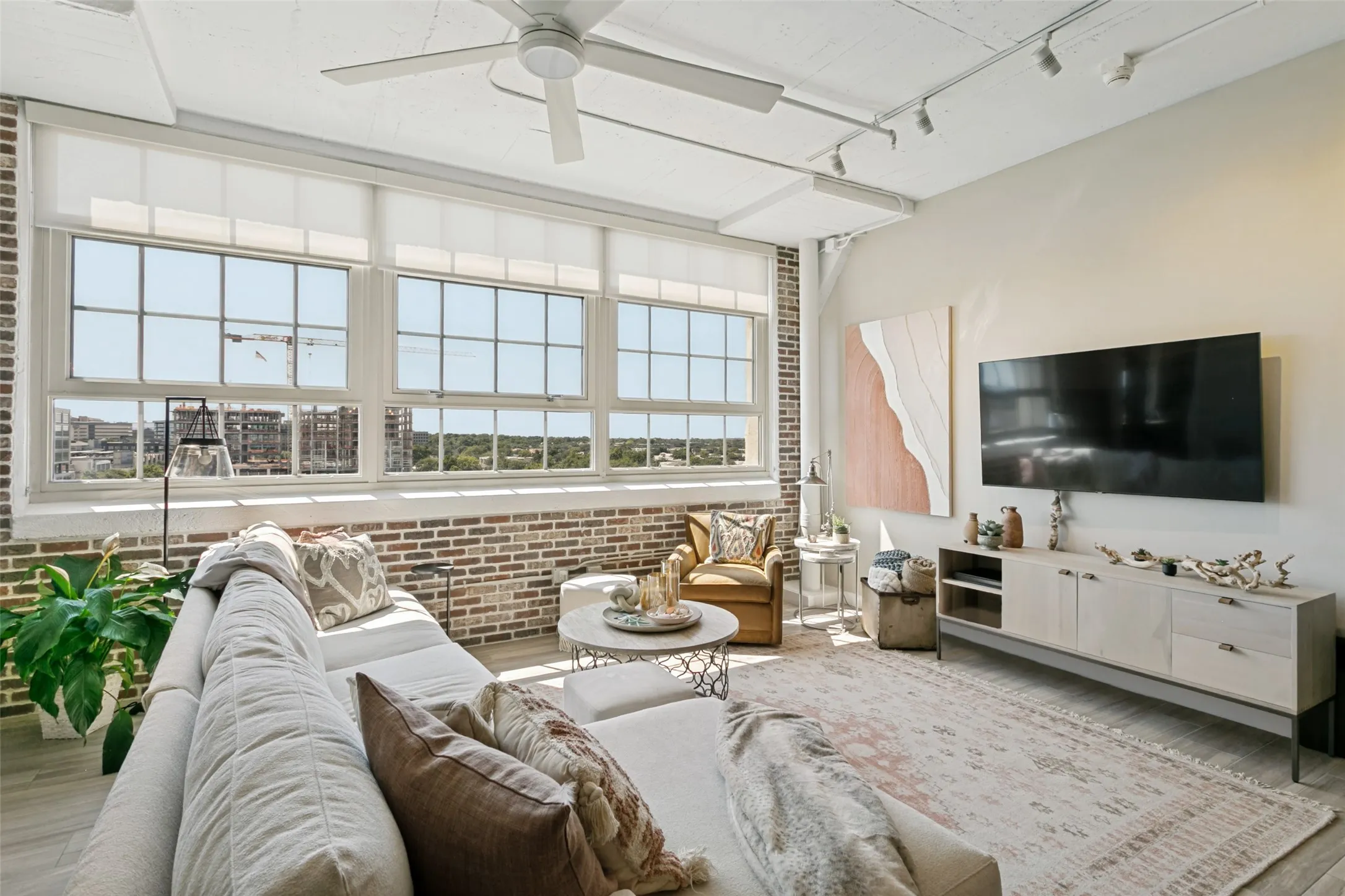 Expansive windows with transom details, exposed brick accents, high ceilings, Minka ceiling fan, and track lighting