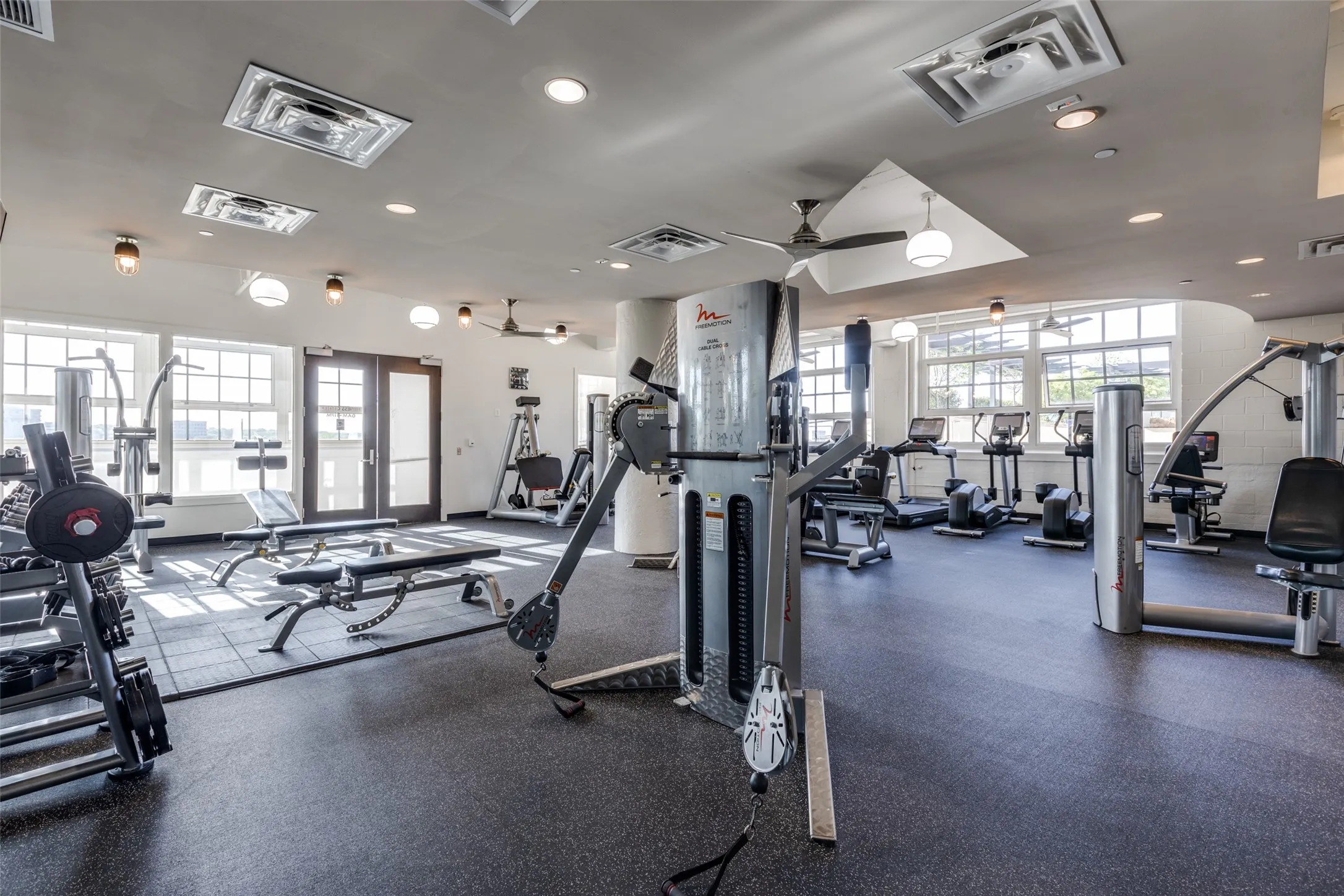 Fitness center with extensive exercise equipment, rubber flooring, and multiple ceiling fans