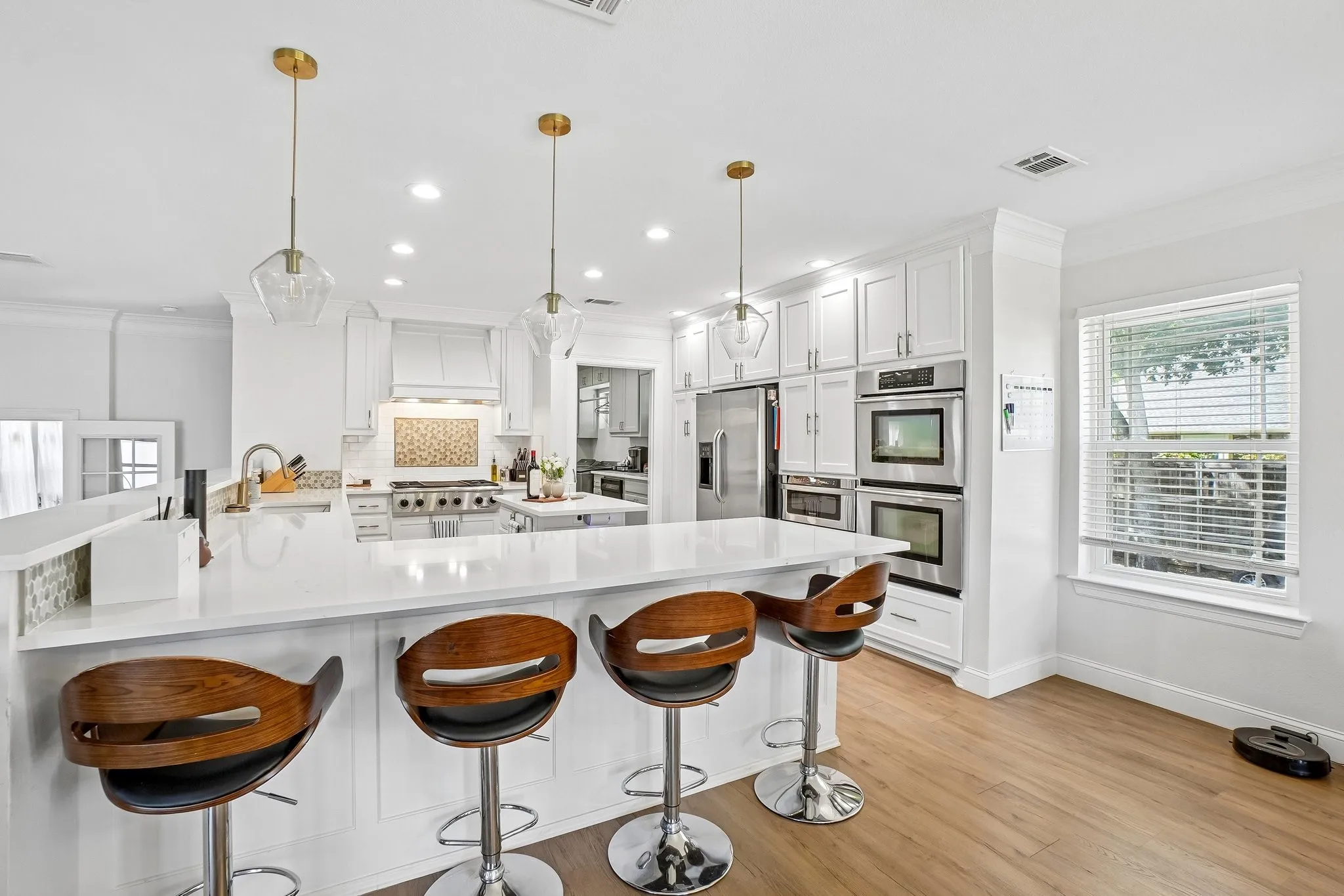 Contemporary kitchen featuring white cabinetry, a waterfall-edge quartz island with seating for four, stainless steel double wall ovens, gas cooktop, and pendant lighting with brass accents