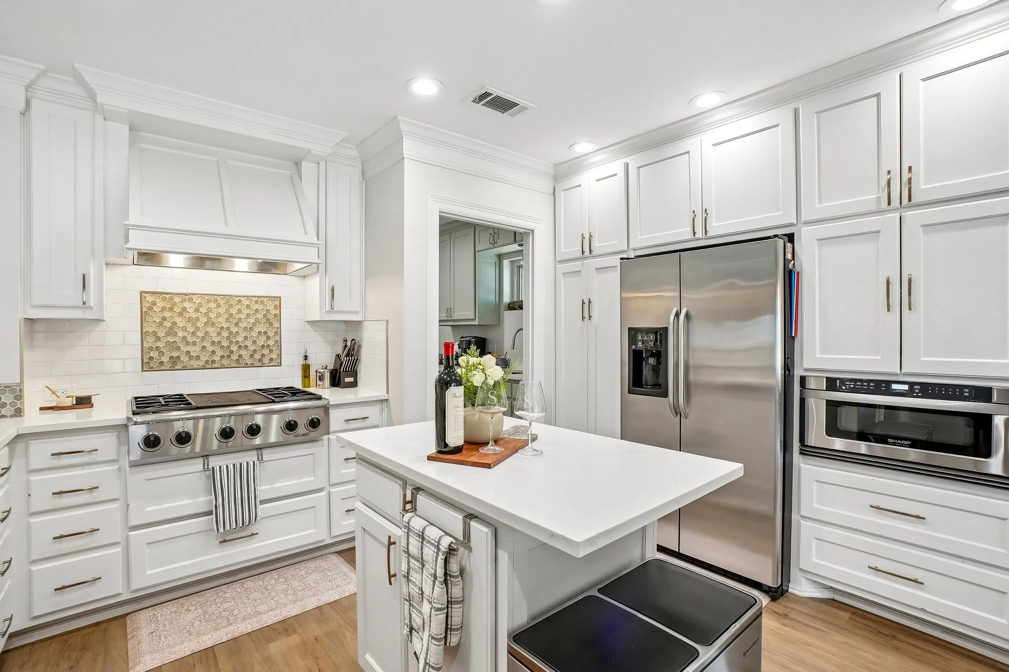 White shaker cabinetry, stainless steel appliances, central island with solid surface countertop, white subway tile backsplash, and wood-finish flooring