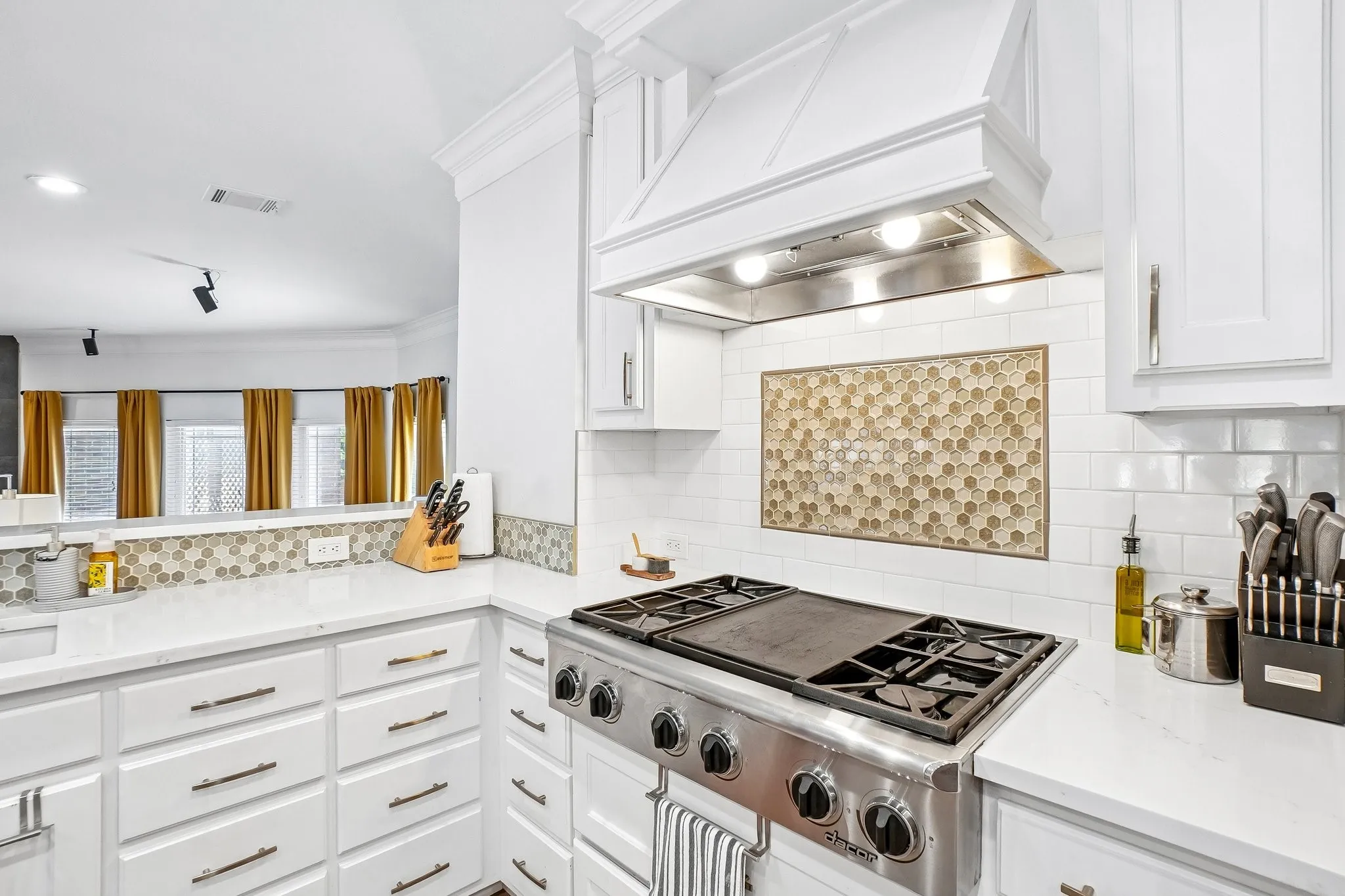 Stainless steel range with griddle, white shaker cabinetry, white subway tile backsplash, hexagonal mosaic tile accent, and light-toned countertops