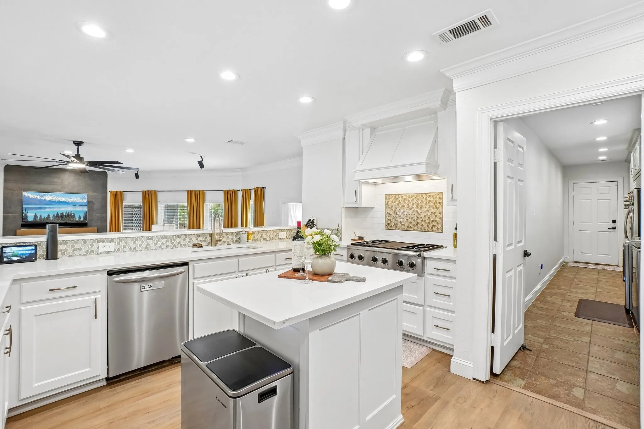 White cabinetry with crown molding, stainless steel appliances, a center island, wood-finish flooring, and a tiled backsplash