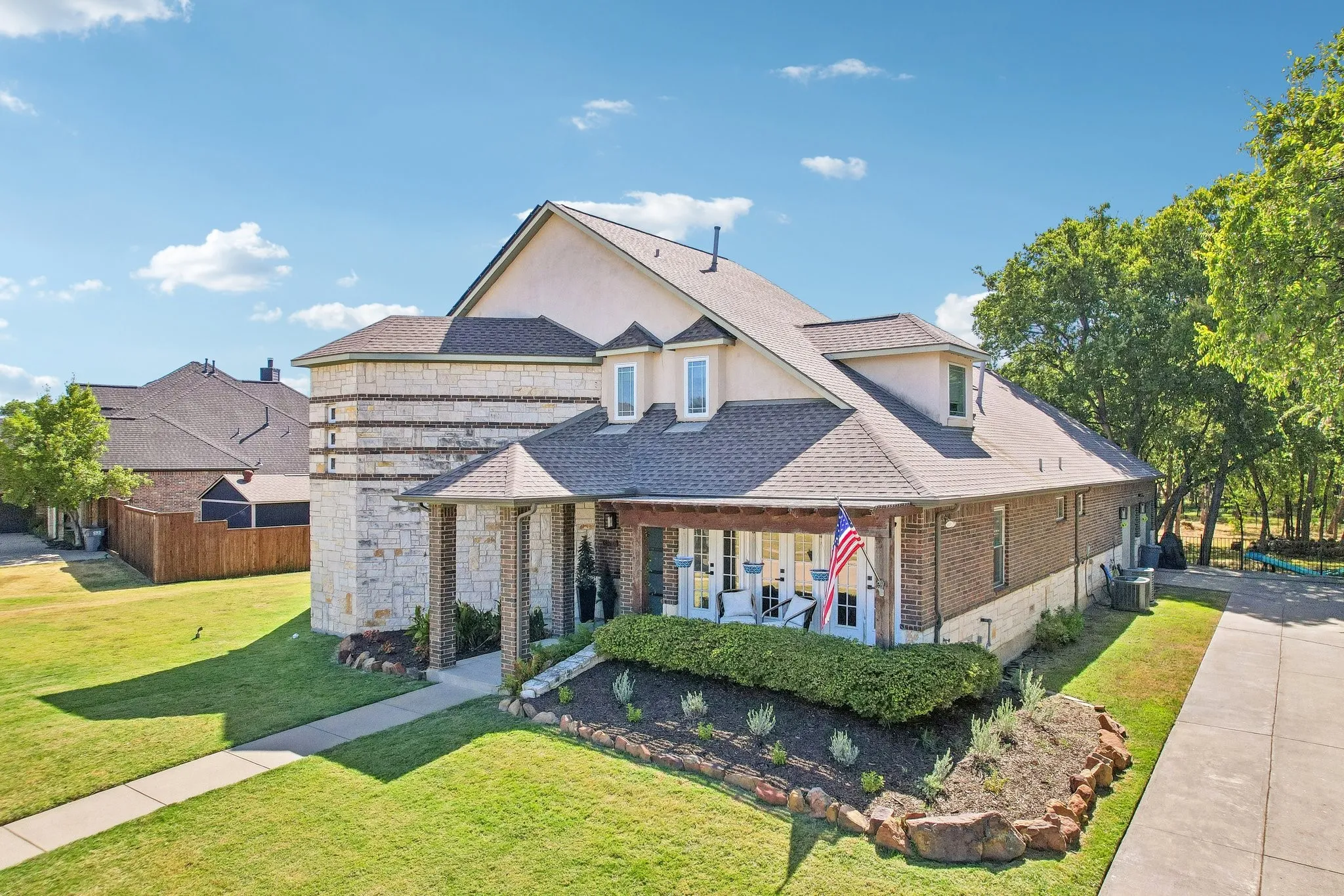 Stone and brick exterior with a covered front porch featuring columns, dormer windows, and a concrete driveway