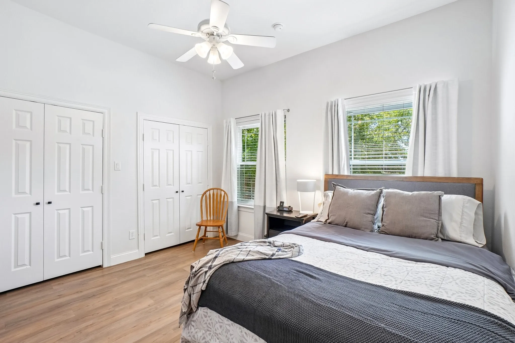 Vaulted ceiling with a ceiling fan, two windows with blinds, two sets of bi-fold closet doors, and wood-finish flooring