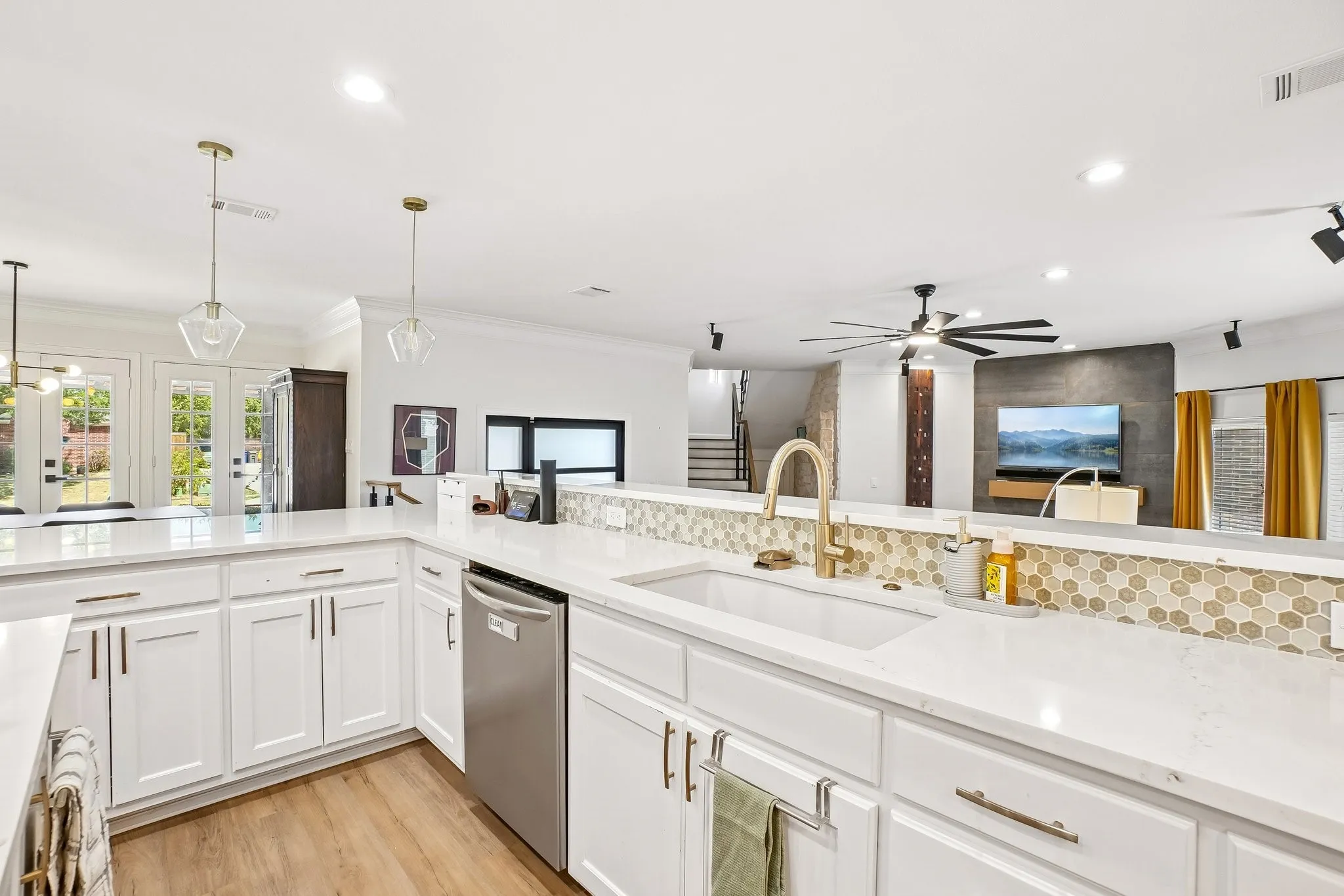 Kitchen featuring white cabinetry, light-toned countertops, a gold-toned faucet, and a hexagonal tile backsplash