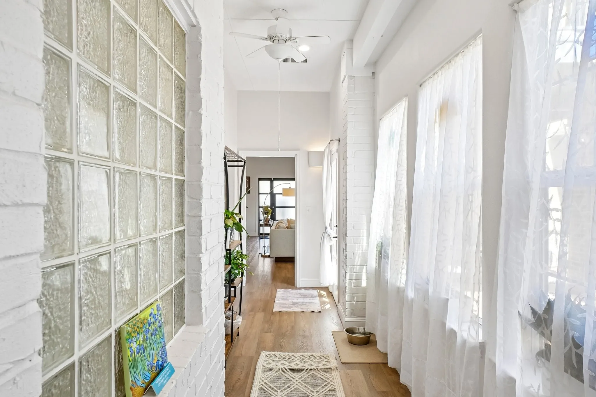 Glass block wall, wood-finish flooring, high ceilings, ceiling fan, and white painted brickwork