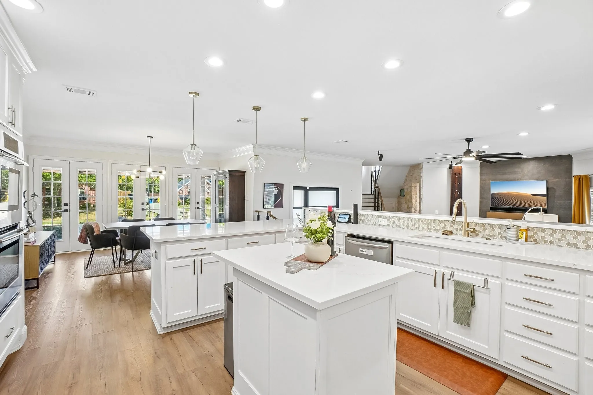 Spacious kitchen featuring two islands with white cabinetry and light-toned countertops, a mosaic tile backsplash, wood-finish flooring, and recessed lighting