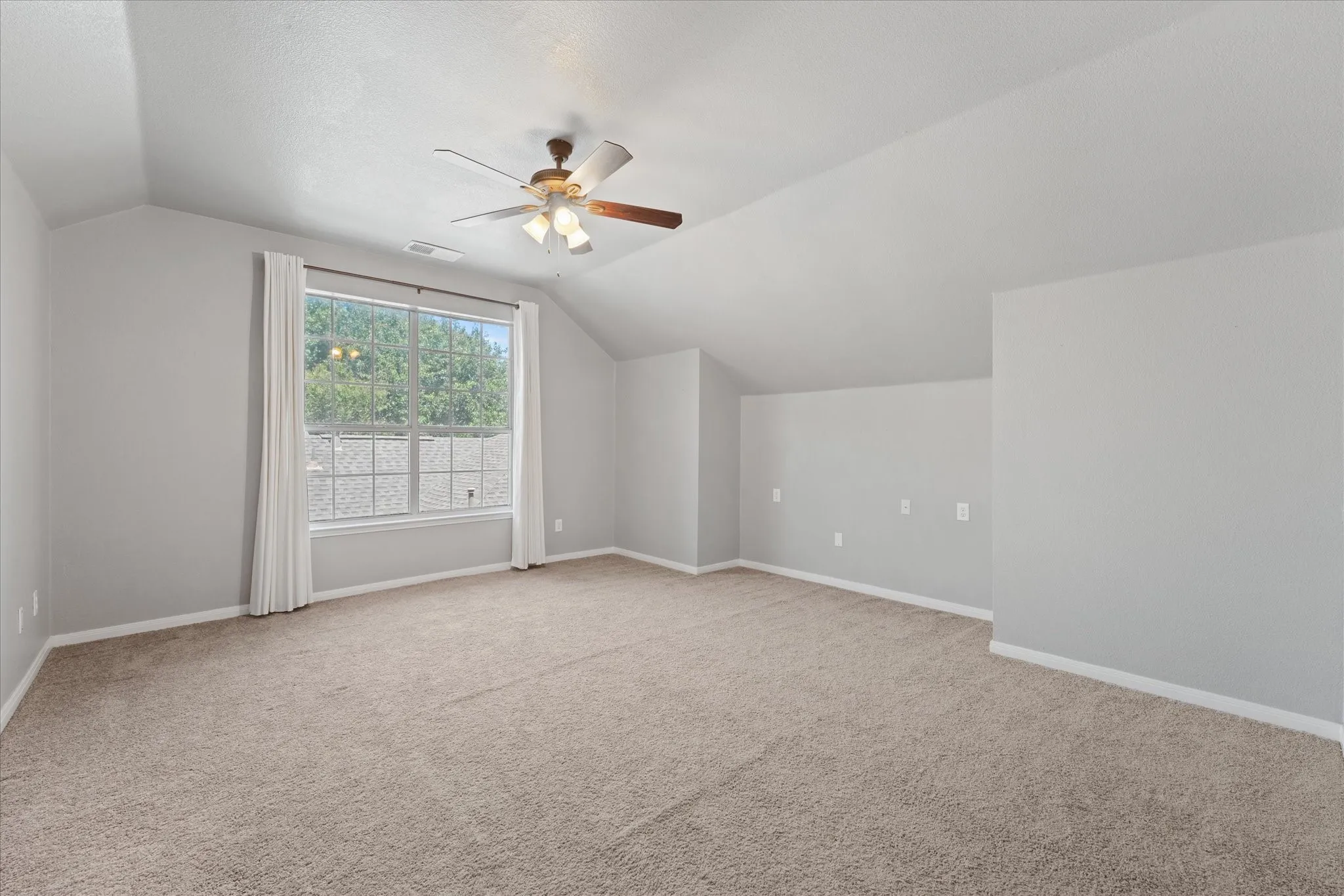 Vaulted ceiling with a ceiling fan, broad window, and neutral carpeting