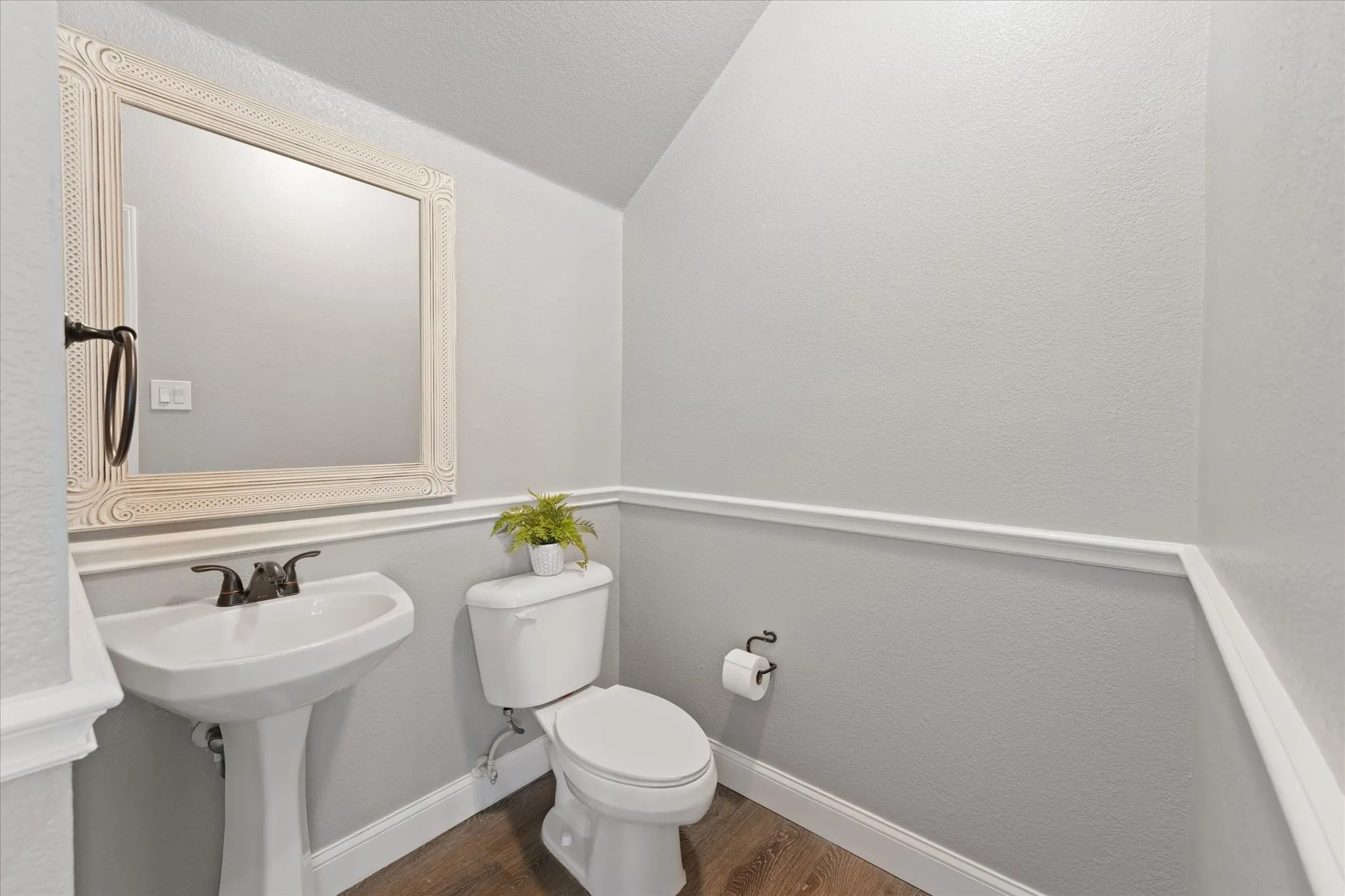 Pedestal sink with bronze-finish faucet, framed mirror, wainscoting, and wood-finish flooring