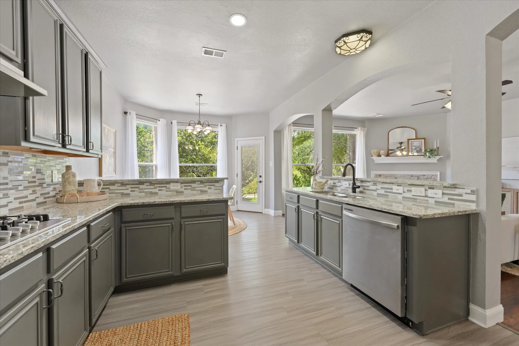 Kitchen featuring gray cabinetry, light-toned countertops, a mosaic tile backsplash, stainless steel appliances, and wood-finish flooring