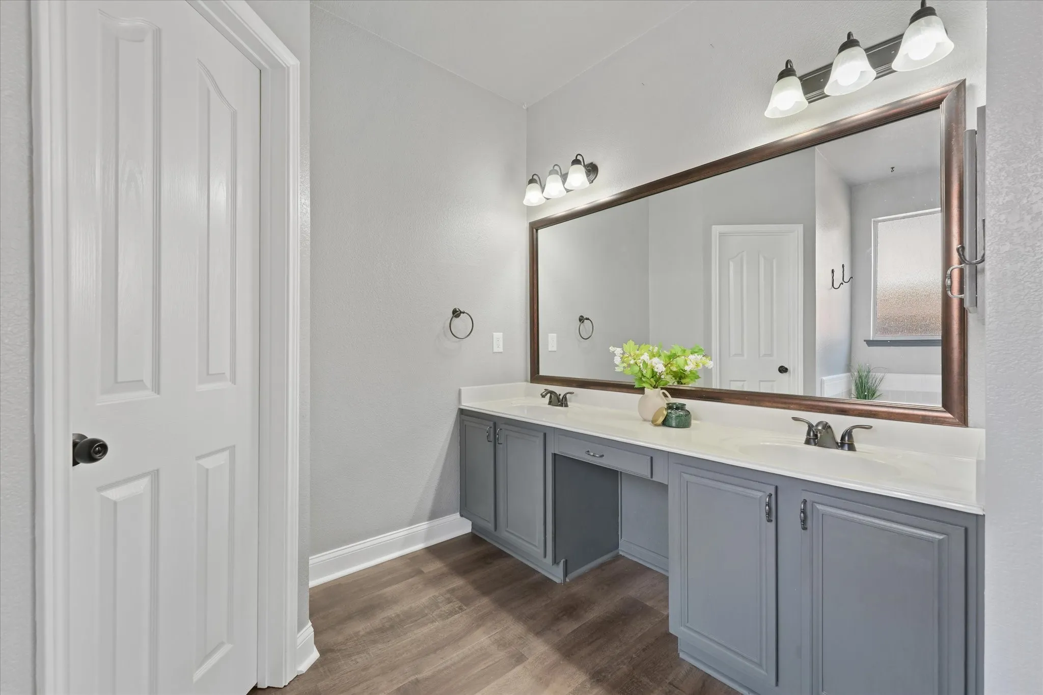 Dual vanity with gray cabinetry, white countertops, a large framed mirror, and wood-finish flooring