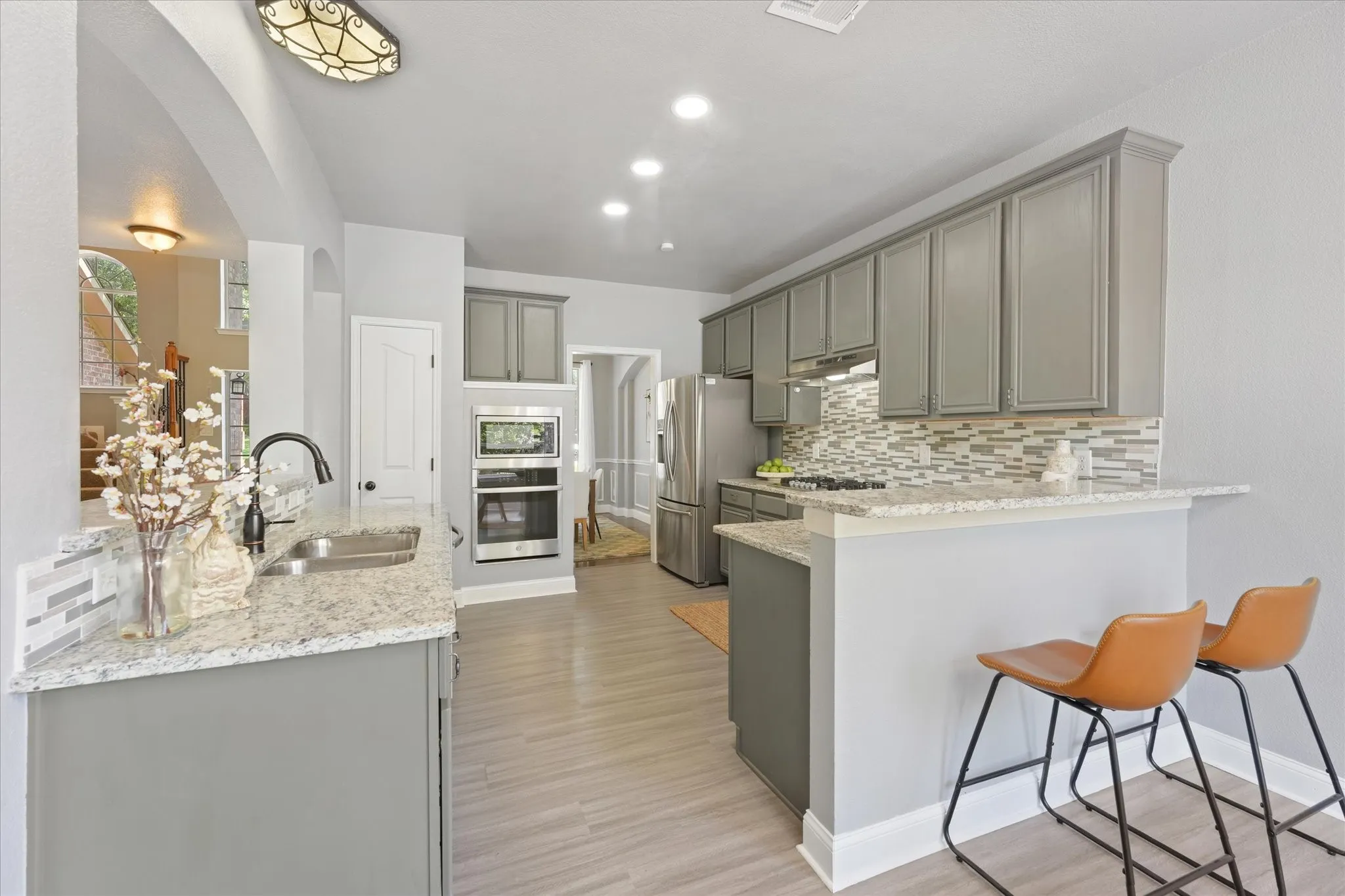 Kitchen featuring gray cabinetry, stainless steel appliances, granite countertops, a tiled backsplash, and wood-finish flooring