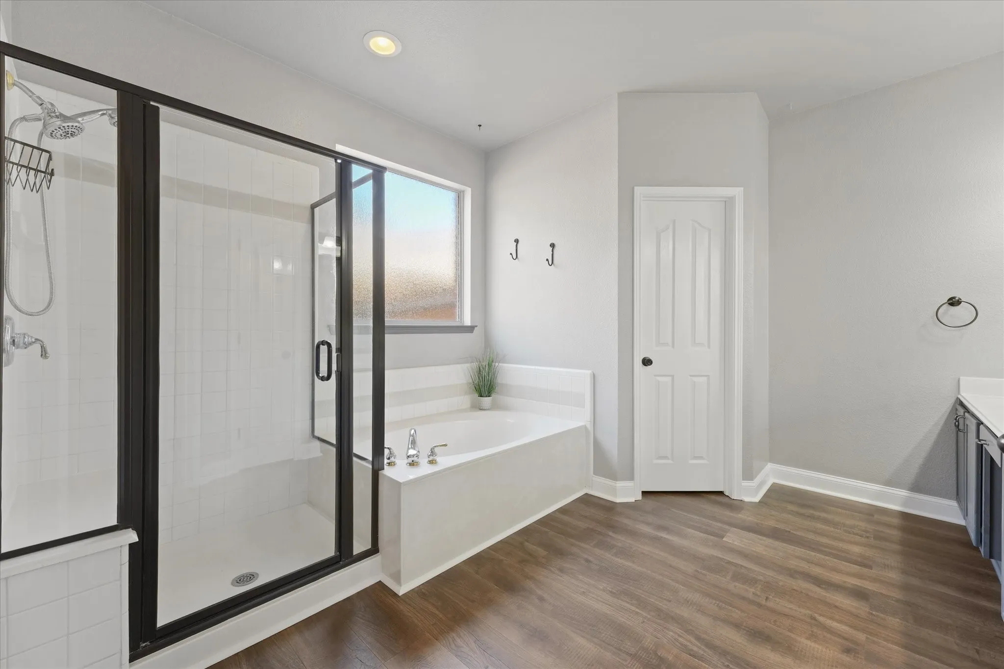 Walk-in shower with black-framed glass enclosure, soaking tub, wood-finish flooring, and white paneled door